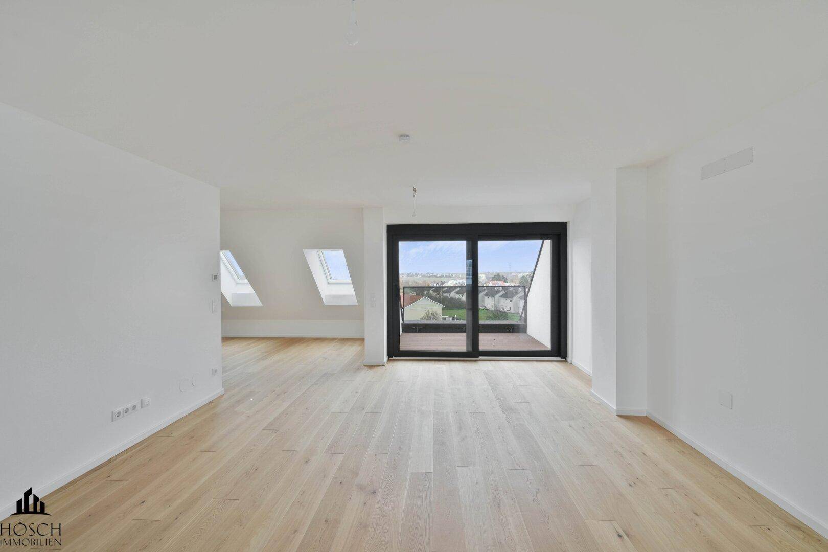 Geräumiger, heller Raum mit Holzboden, Dachschrägen, Dachfenstern und Zugang zu einem Balkon.