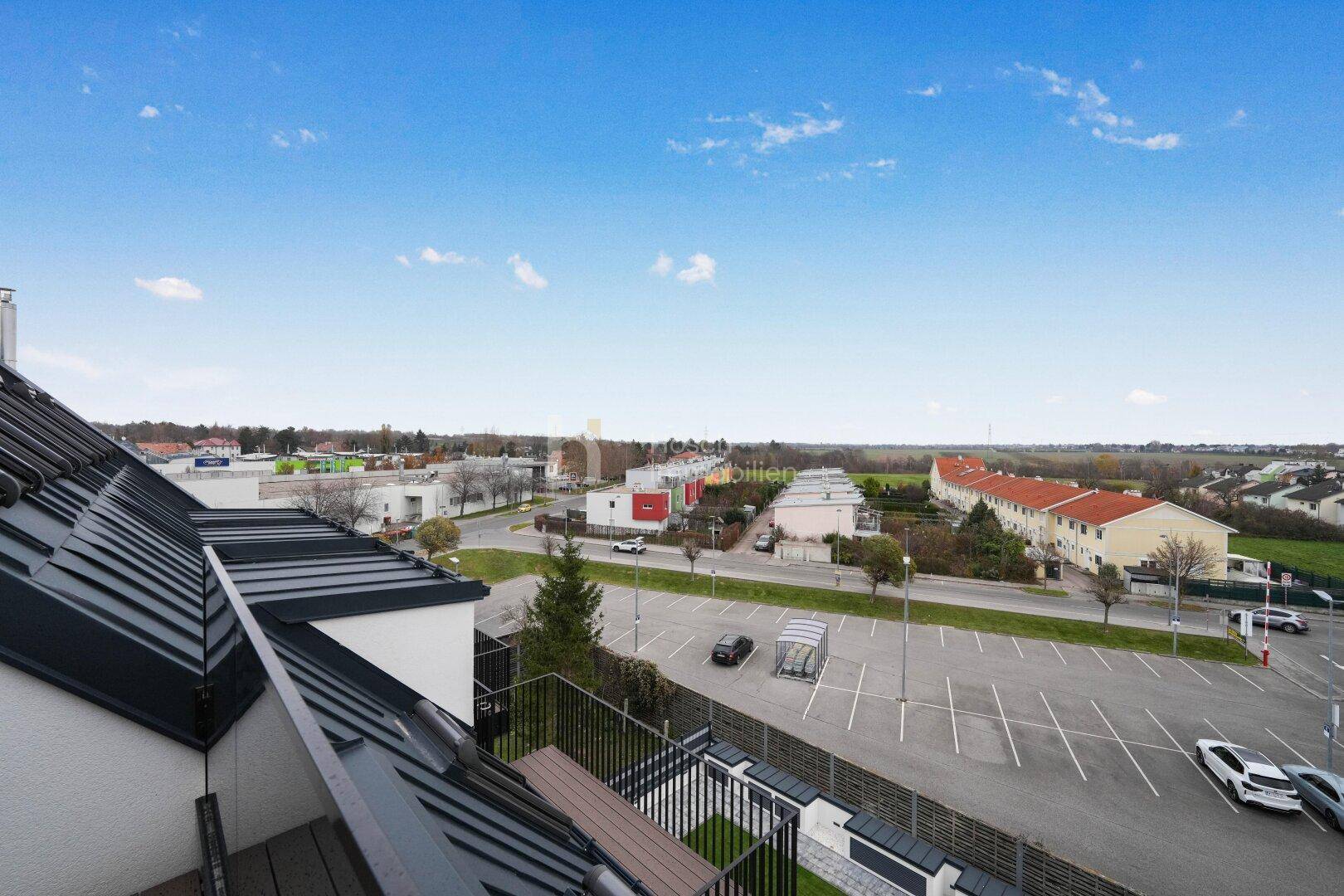 Weitblick vom Balkon über die Umgebung mit Parkplätzen und angrenzender Landschaft.