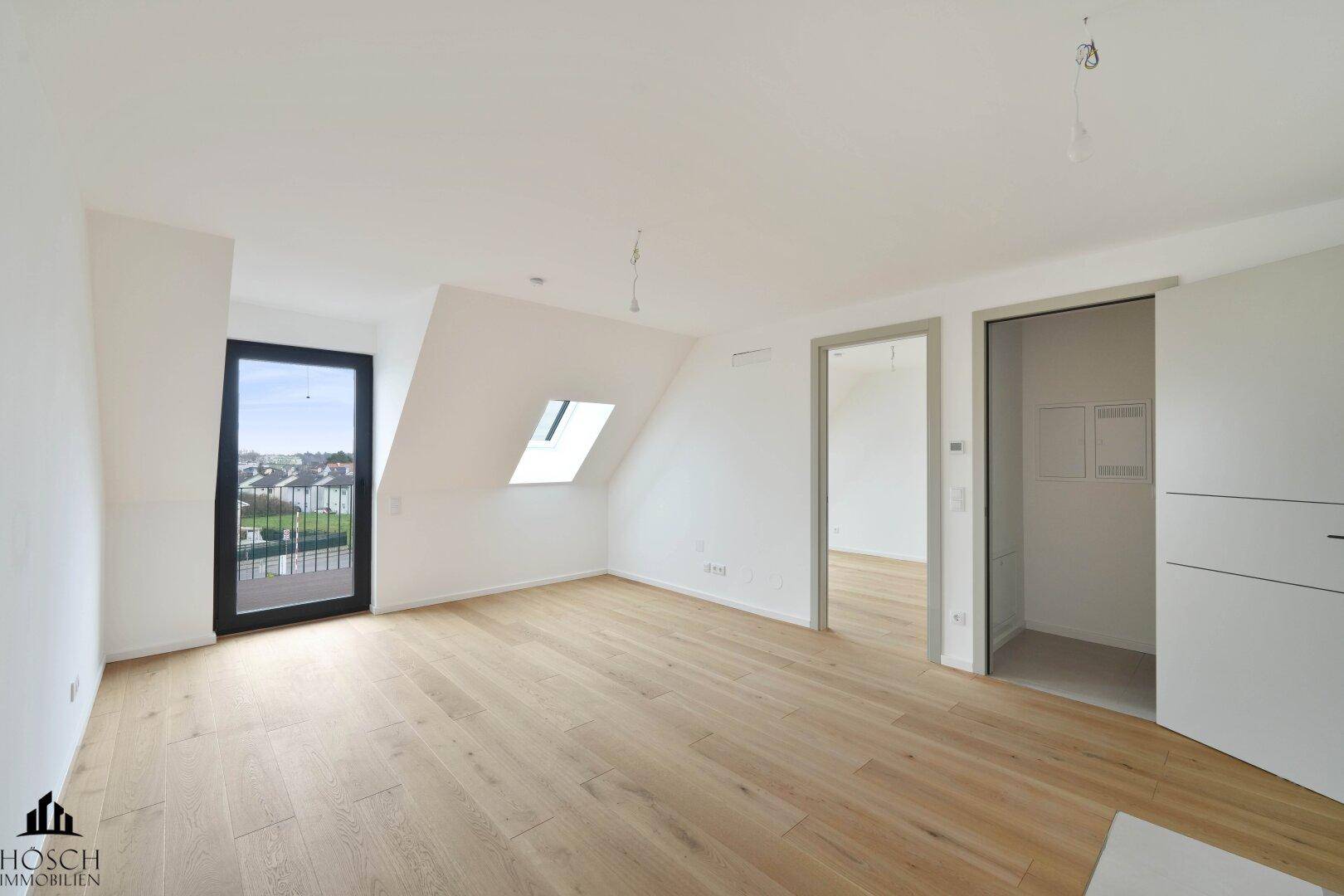 Heller, leerer Raum mit Holzboden, Balkonzugang, Dachschräge und integriertem Abstellbereich.