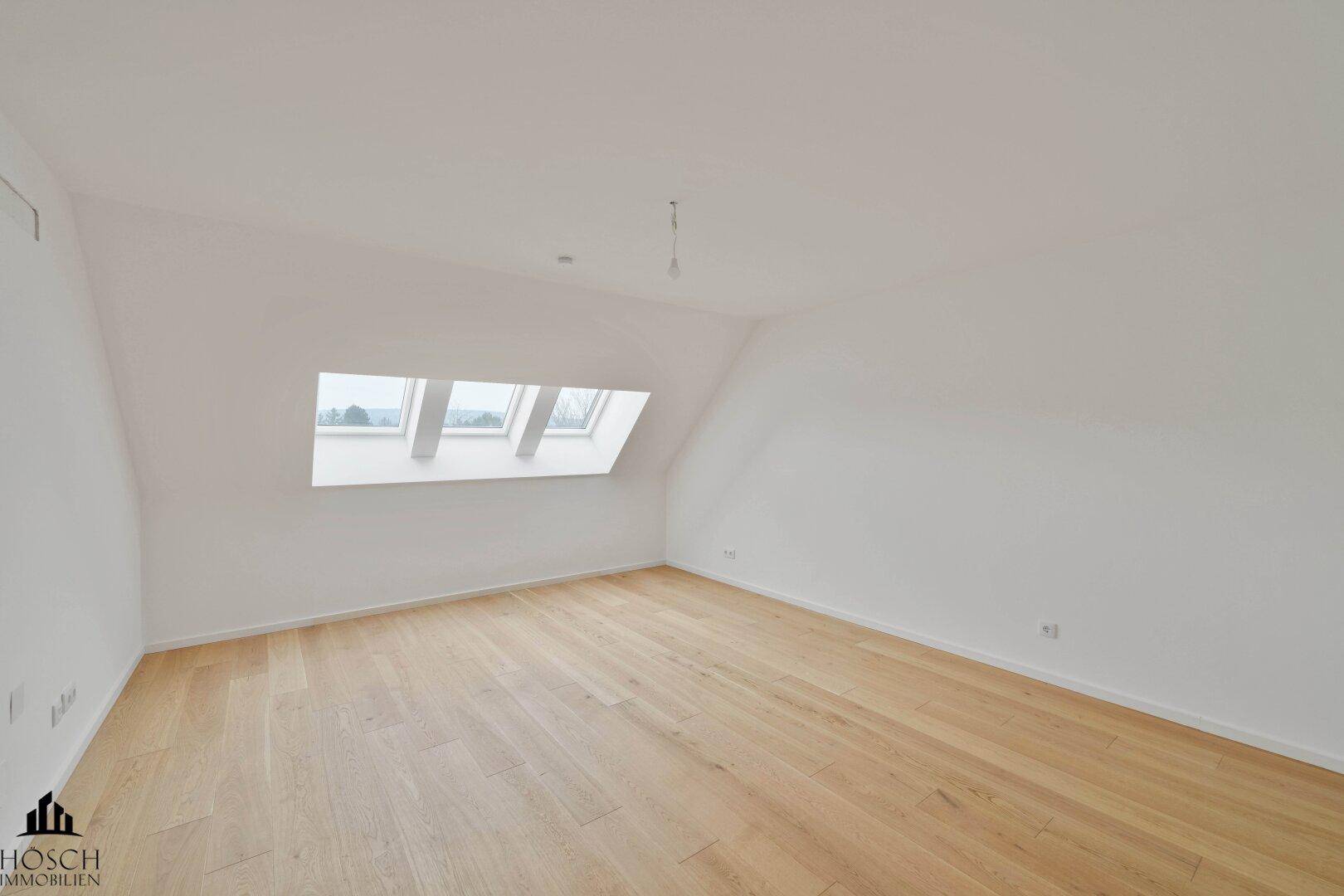 Heller, leerer Raum mit Holzboden, Dachschrägen und zwei Dachfenstern.