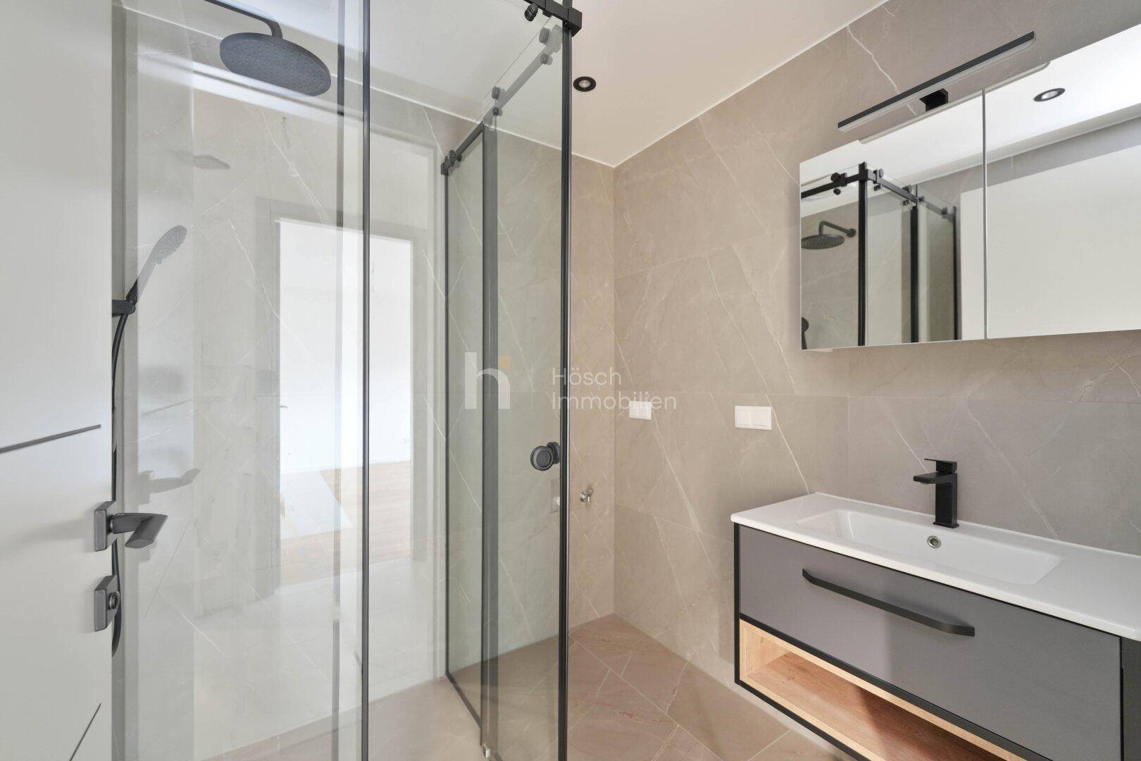 Modernes Badezimmer mit begehbarer Dusche, eleganten Fliesen und Waschtisch mit Spiegelschrank.