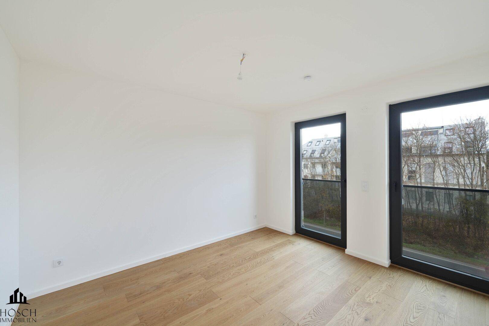 Heller, leerer Raum mit Holzboden und zwei französischen Balkonen.