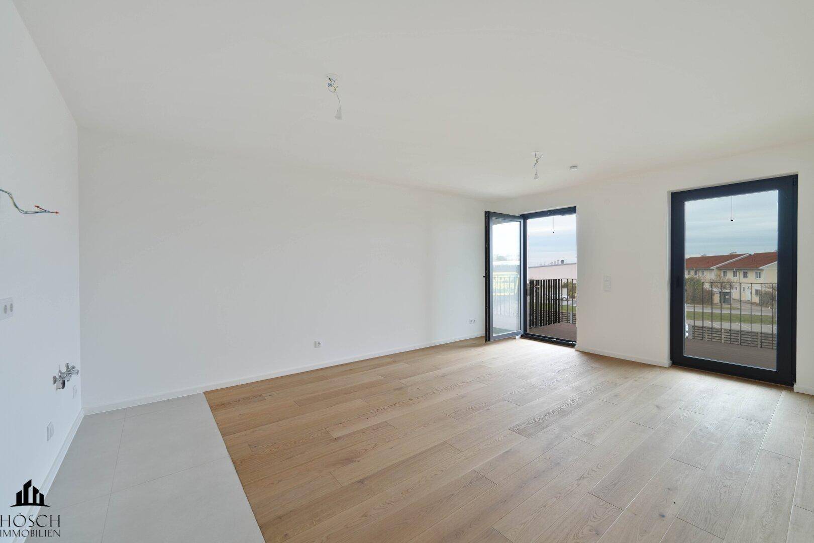 Geräumiger, heller Raum mit Holzboden und zwei Balkonzugängen.