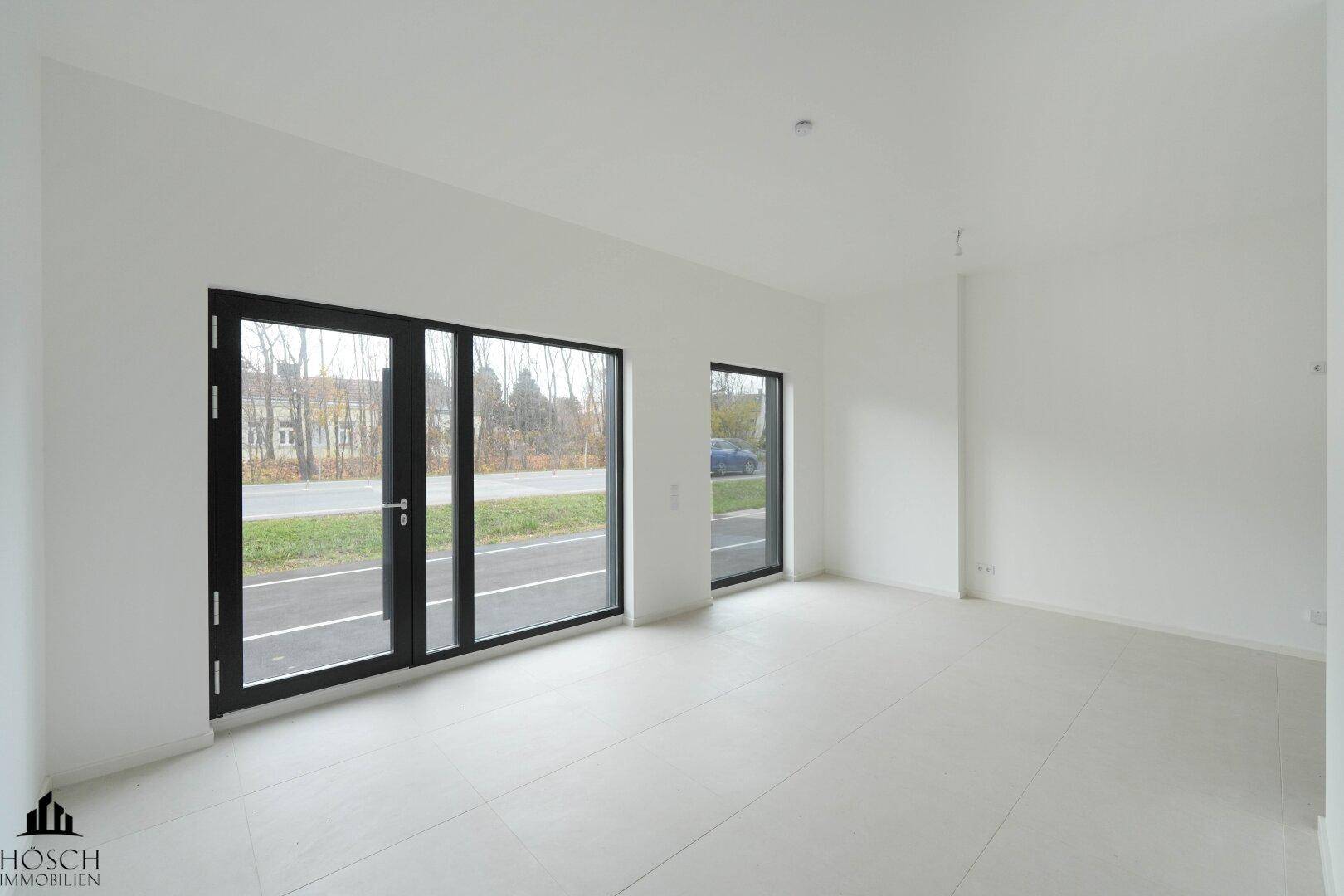 Heller, leerer Raum im Erdgeschoss mit großen Fenstern und Fliesenboden.