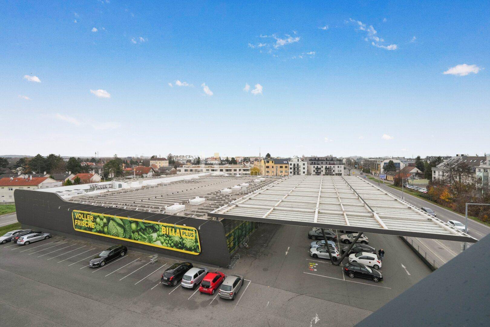 Luftaufnahme eines Supermarktes mit großem Parkplatz und umliegender städtischer Infrastruktur.