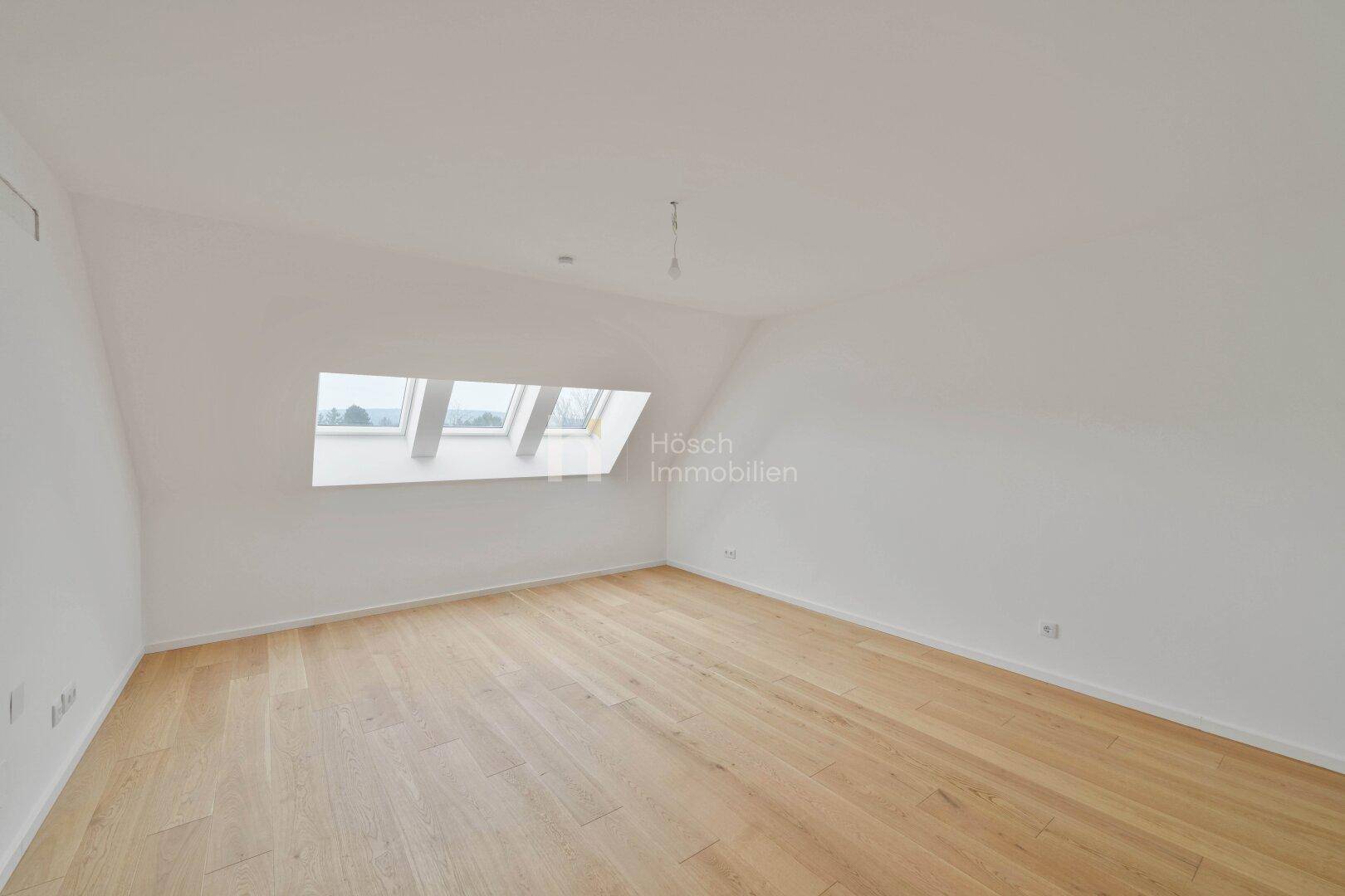 Geräumiges Schlafzimmer im Dachgeschoss mit Holzboden und großen Dachfenstern.