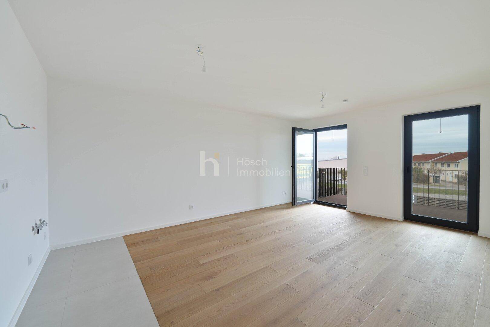 Heller Wohnbereich mit Holzboden und großen Fenstertüren, die zu einem Balkon führen.