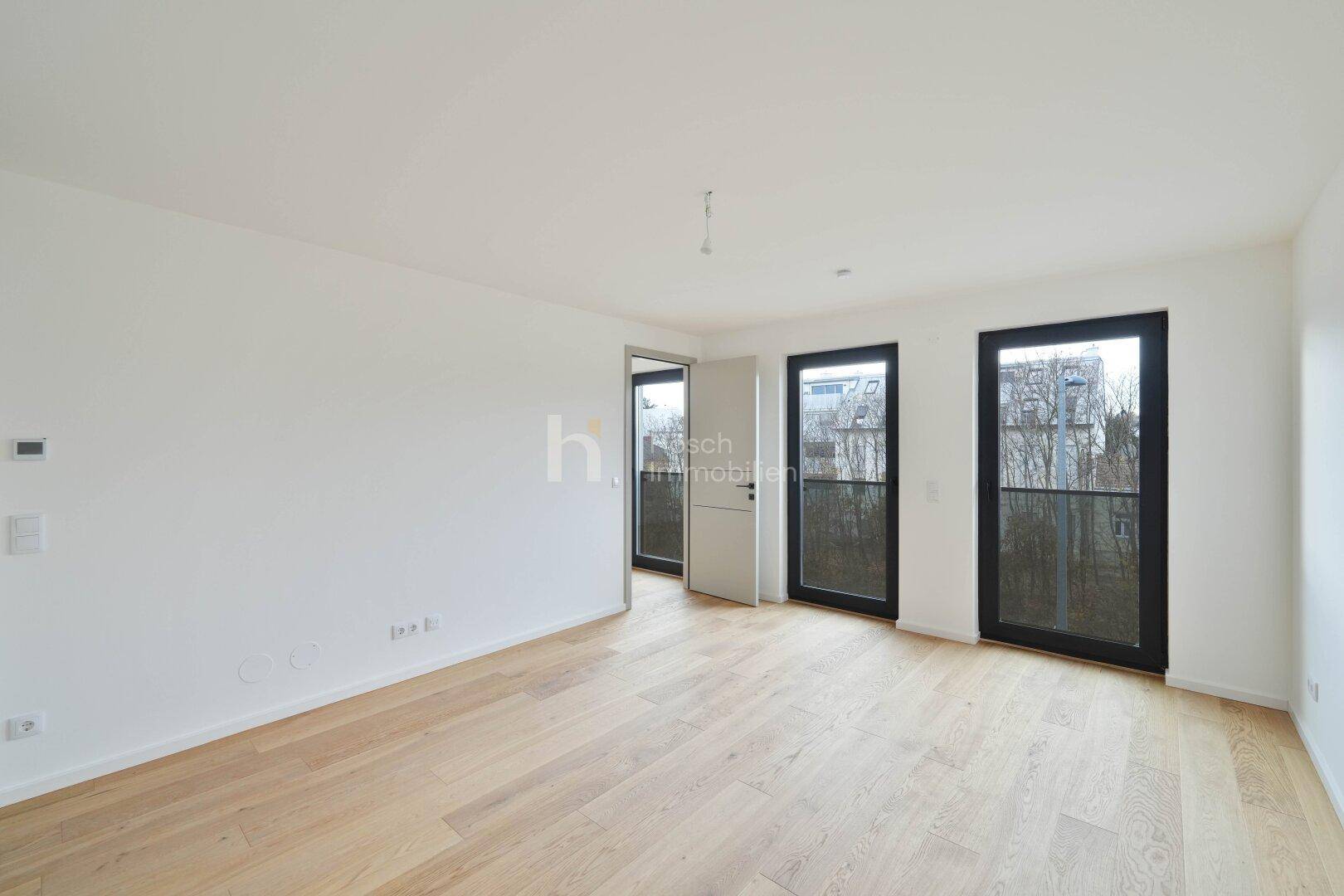 Geräumiger, heller Wohnbereich mit Holzboden und mehreren Fenstertüren, die zum Außenbereich führen.