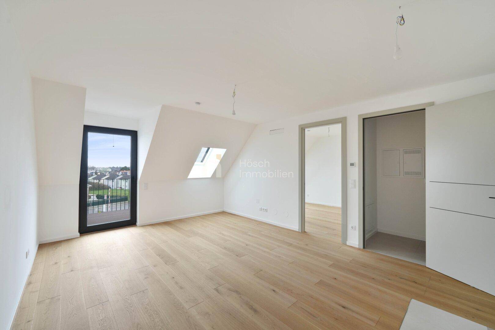 Geräumiger Wohnbereich mit Holzboden, Dachfenster und Zugang zu einem weiteren Raum.