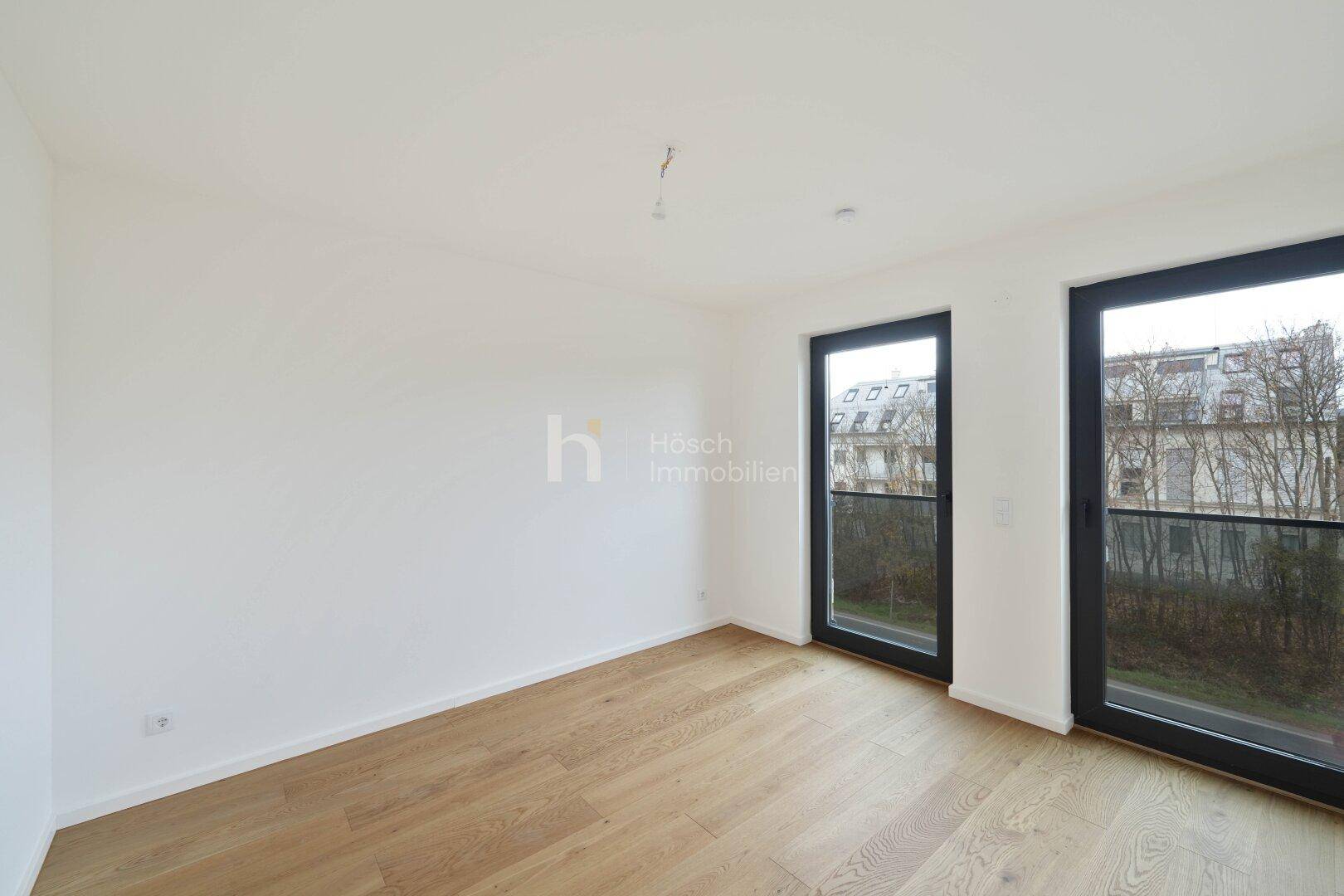 Helles Schlafzimmer mit Holzboden und zwei großen Fenstertüren, die viel Tageslicht hereinlassen.
