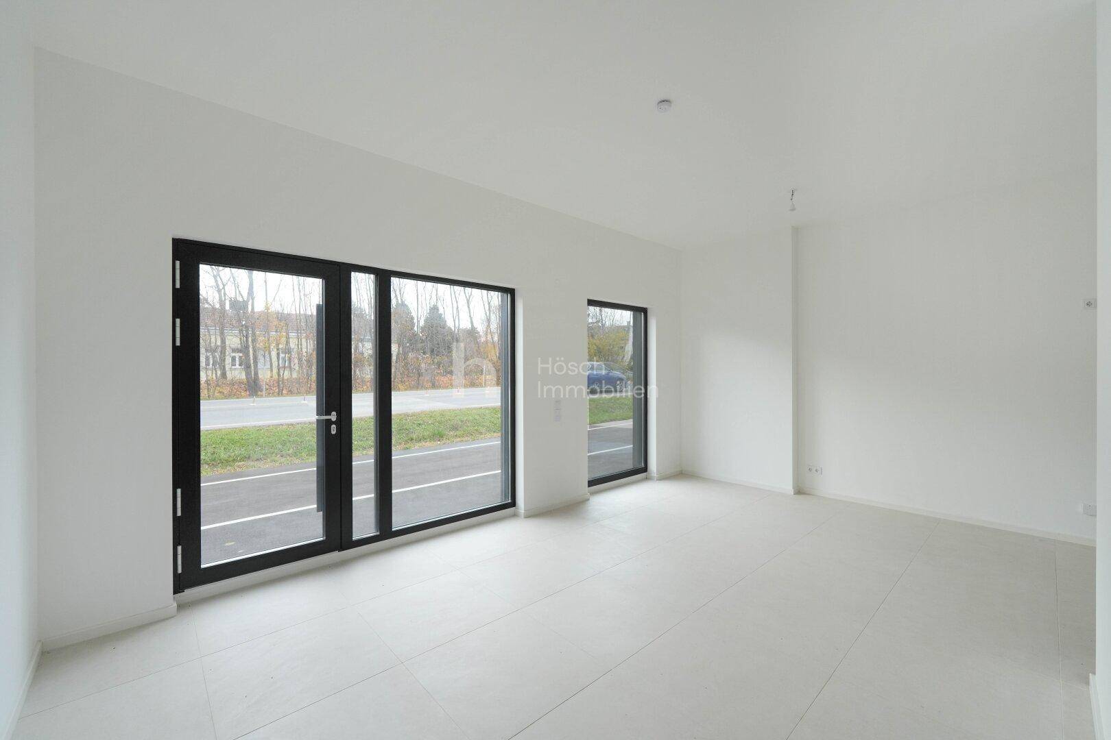 Heller Wohnbereich im Erdgeschoss mit Fliesenboden und großen Fenstern zur Straße hin.