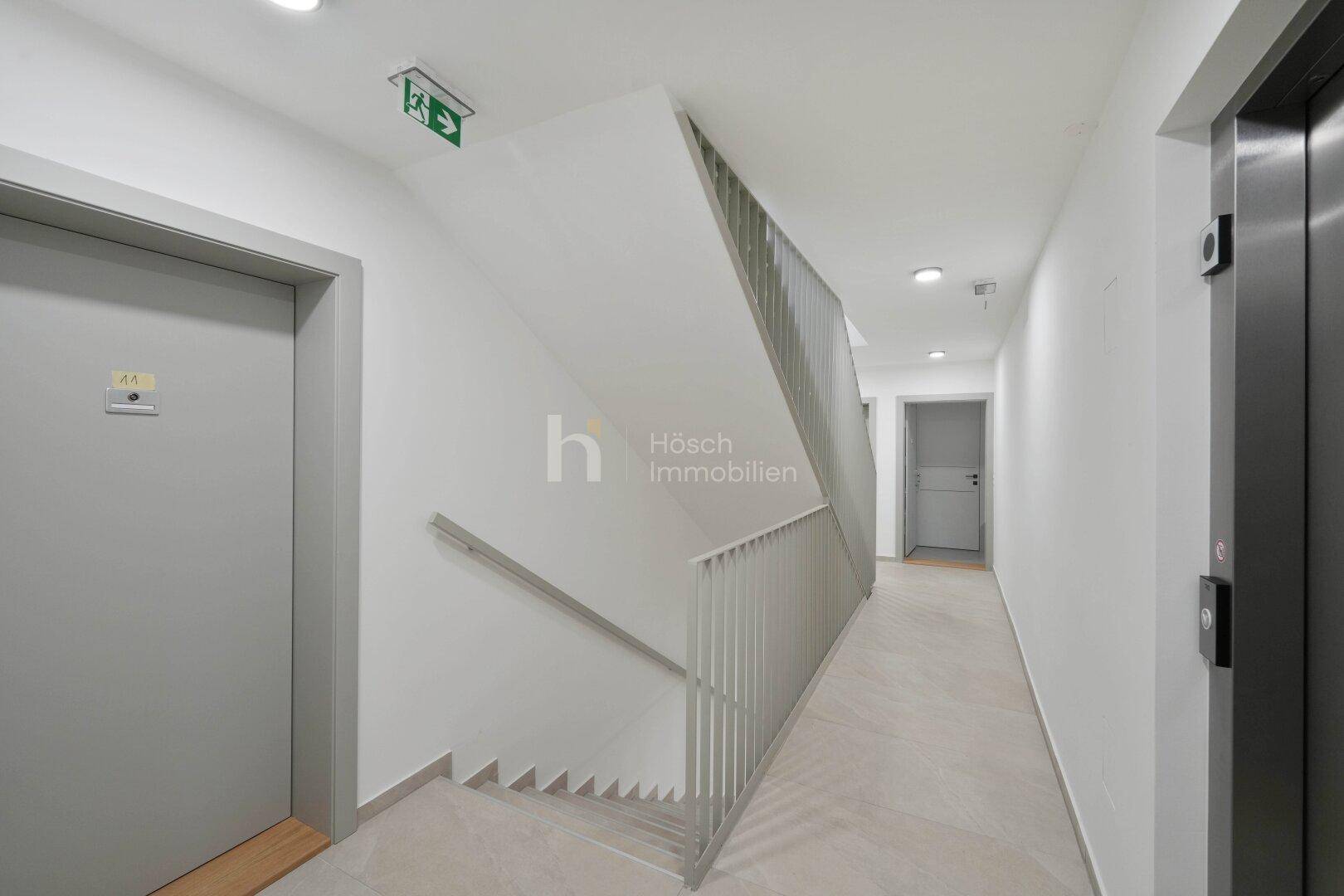 Heller Flur mit Treppenhaus und Aufzug, der Zugang zu den verschiedenen Etagen bietet.