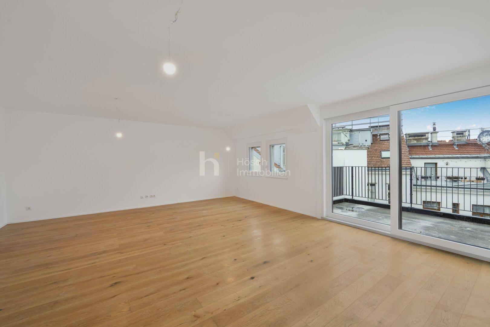 Heller, unmöblierter Wohnraum mit Holzboden und großen Fenstern, die viel Tageslicht hereinlassen.