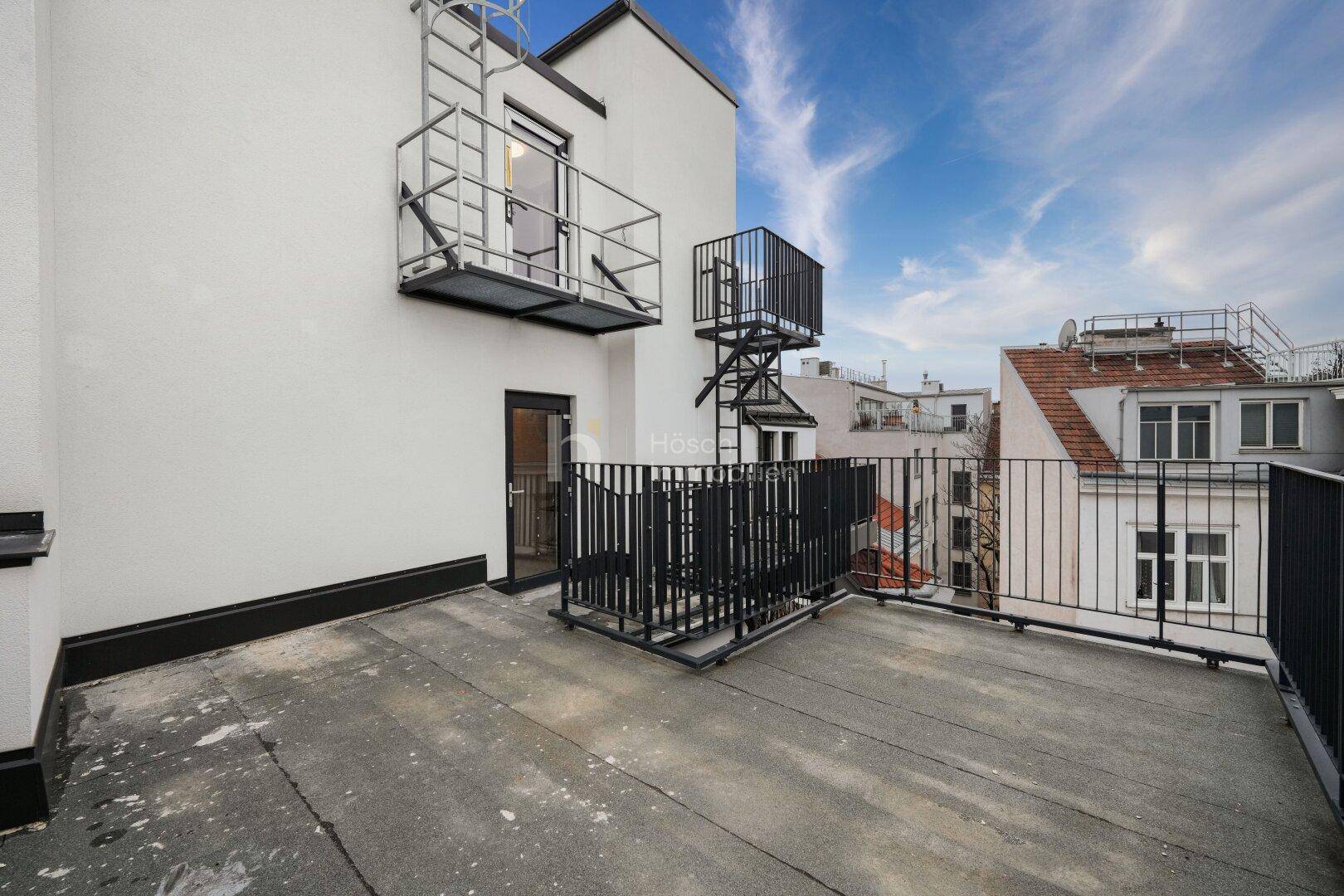 Geräumige Dachterrasse mit Metallgeländer und Blick über die Dächer der Stadt.