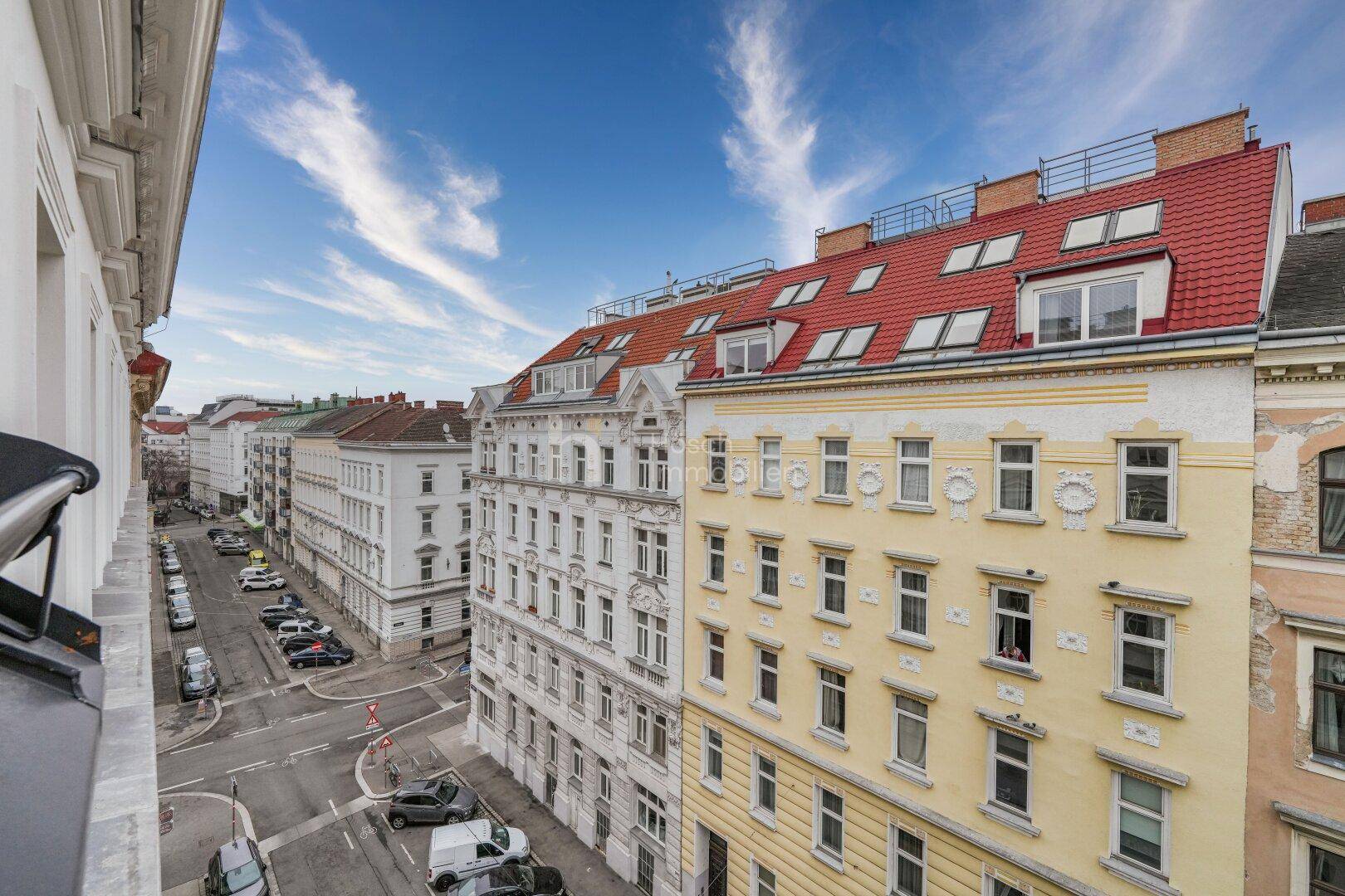 Blick von oben auf eine belebte Stadtstraße mit historischen Gebäuden und Dächern.