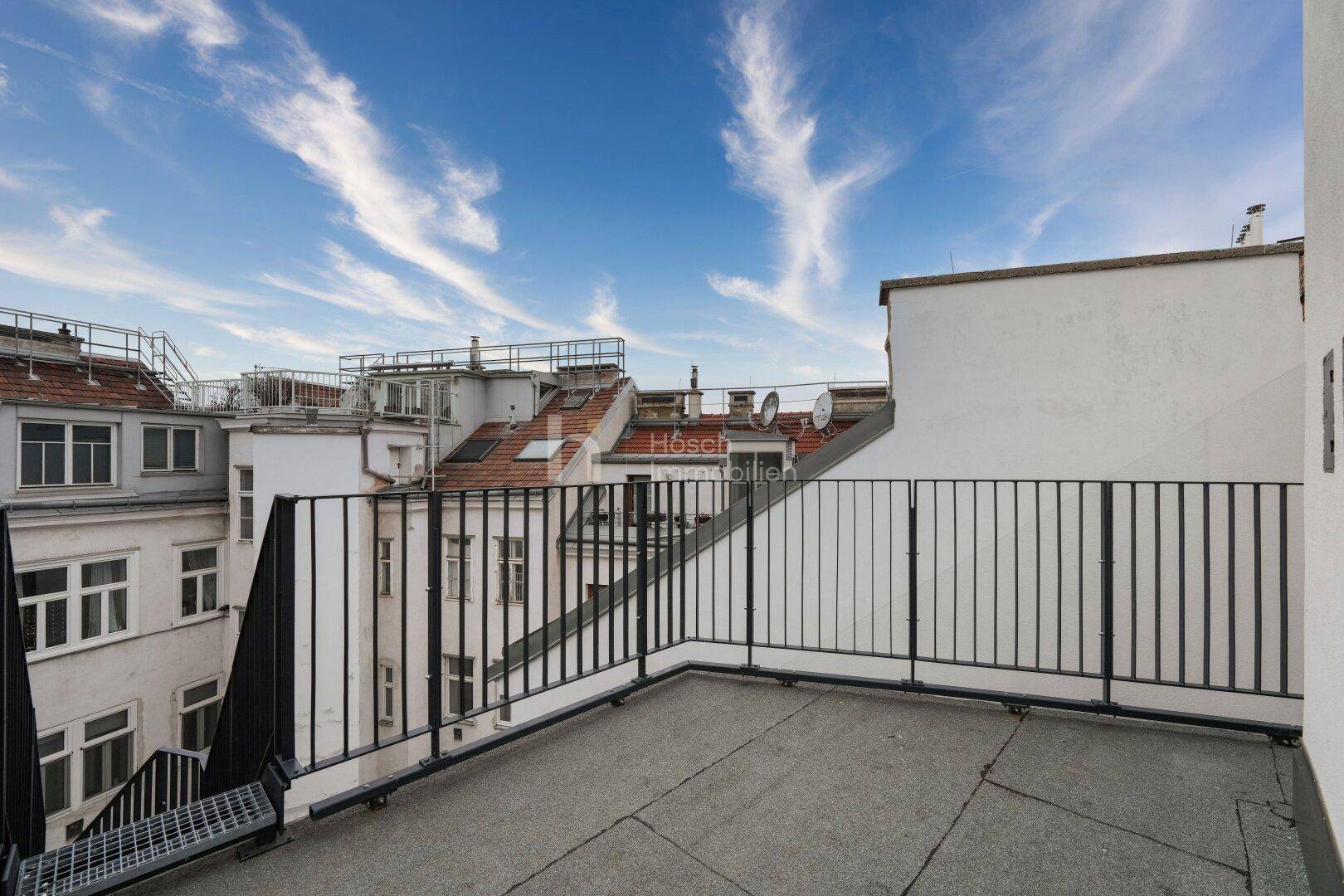 Weitläufige Dachterrasse mit einem weiten Blick über die Dächer der Stadt unter blauem Himmel.