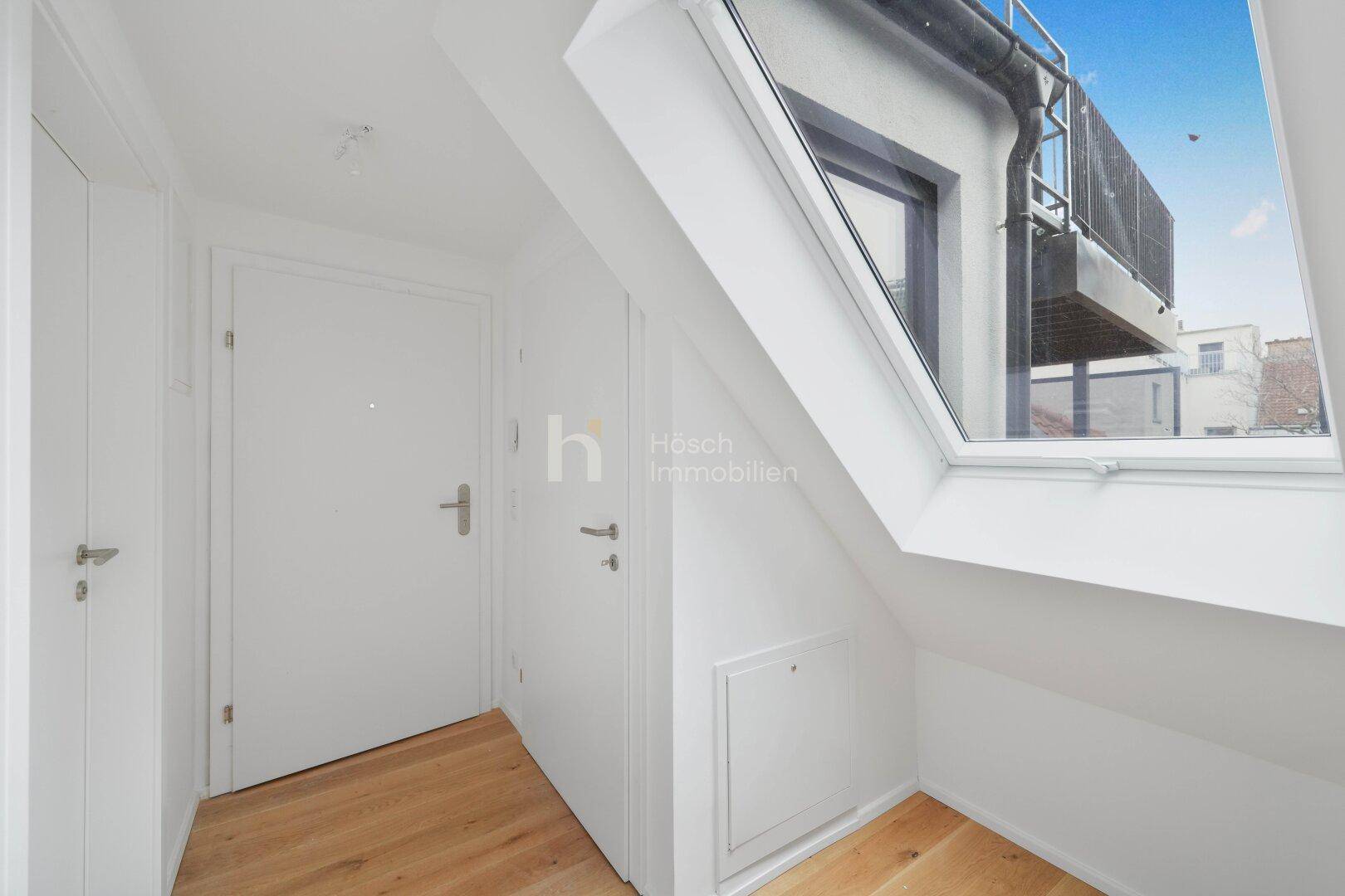Heller Flur im Dachgeschoss mit Holzfußboden und einem großen Dachfenster, das Tageslicht hereinlässt.
