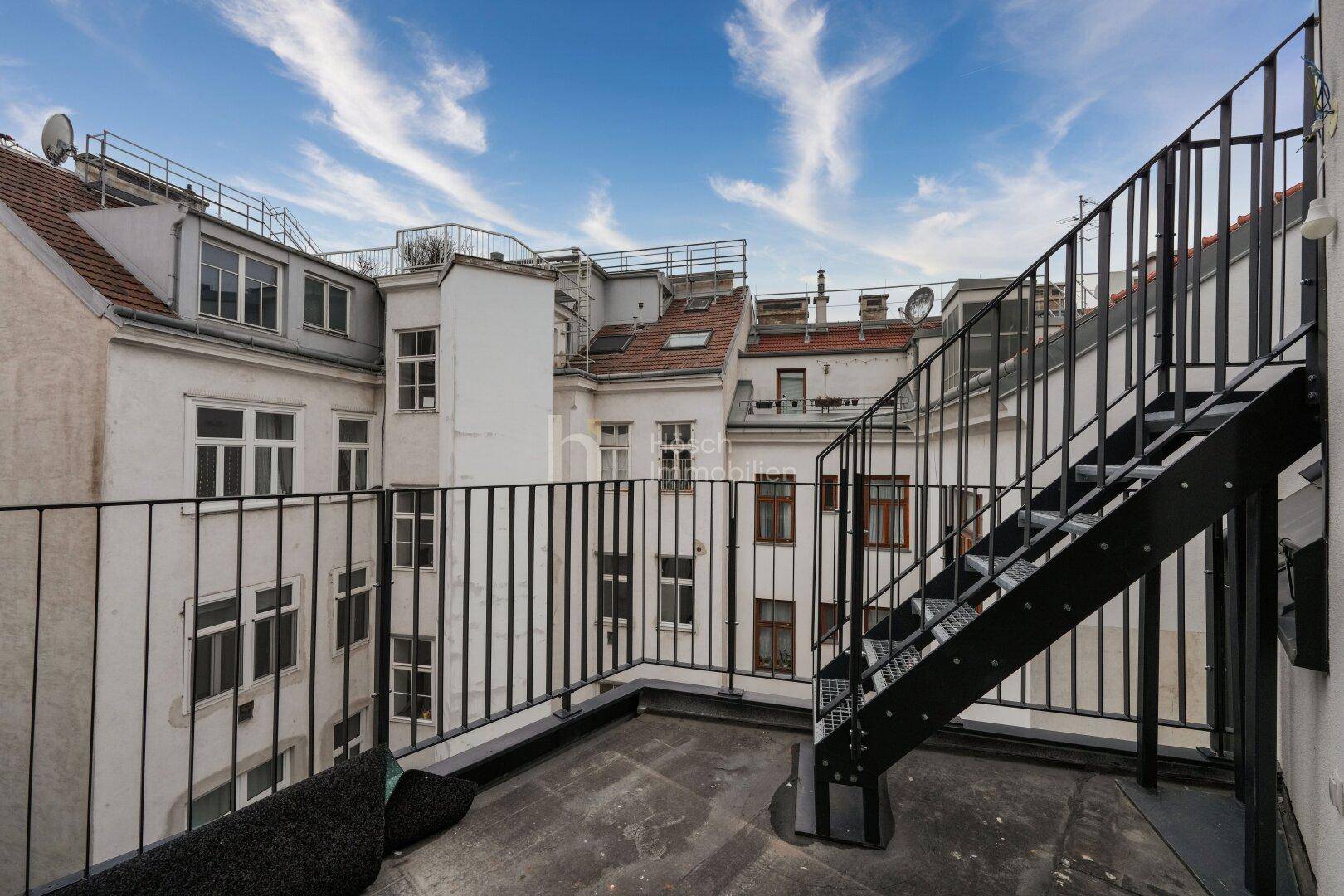 Dachterrasse mit Metallgeländer und Blick auf die umliegenden Gebäude und den blauen Himmel.