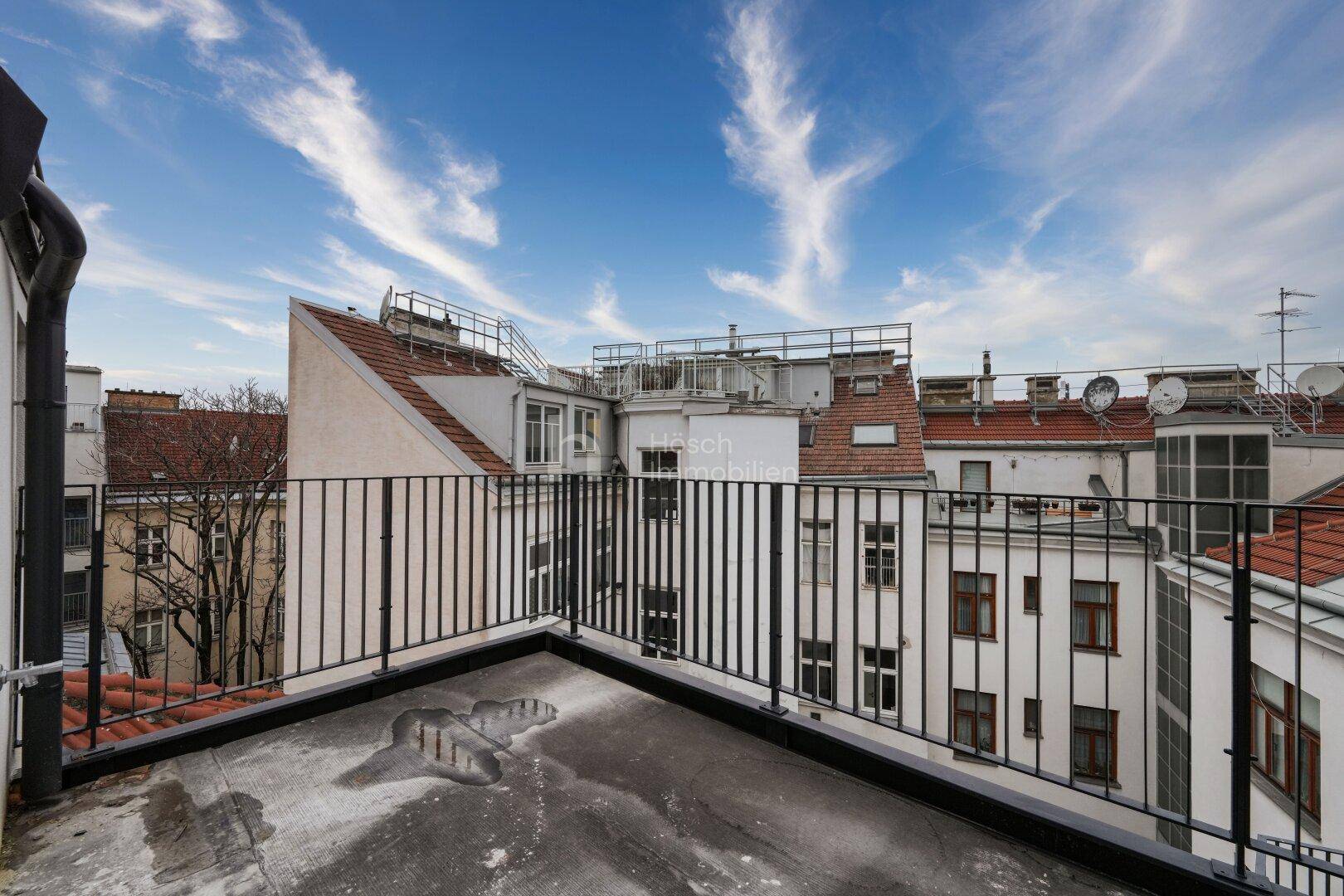 Geräumige Dachterrasse mit schwarzem Geländer und weitem Blick über die umliegenden Dächer der Stadt.