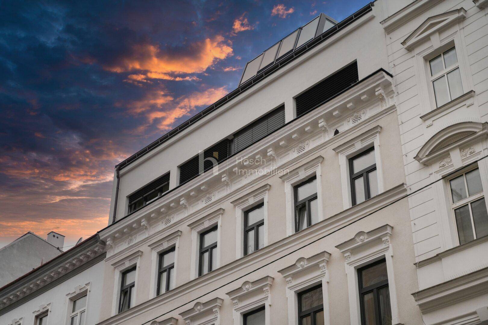 Historische Fassade mit Stuckelementen und modernem Dachausbau unter einem dramatischen Abendhimmel.