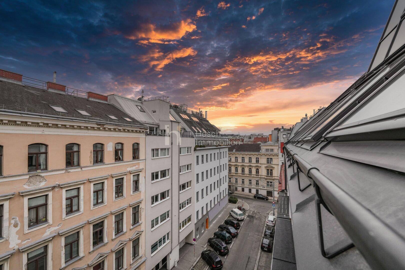 Blick über die Dächer der Stadt bei Sonnenuntergang, mit angrenzenden Gebäuden und Straße.
