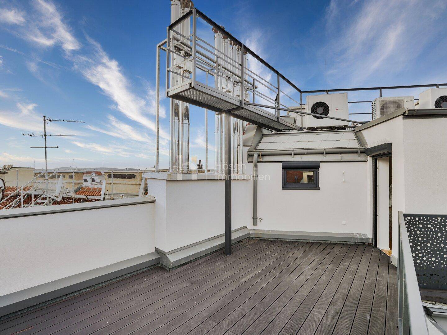 Dachterrasse mit Holzdielen, Klimaanlagen und weitem Blick über die umliegenden Dächer der Stadt.