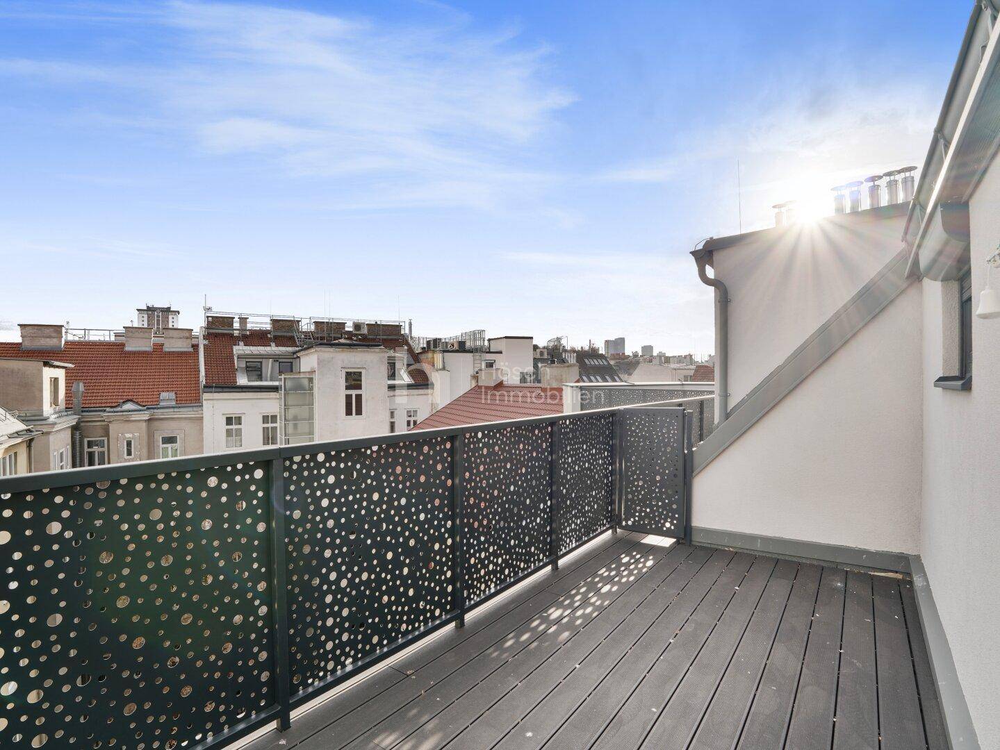 Sonnige Dachterrasse mit Holzdielen und modernem Lochblechgeländer, ideal für Outdoor-Aktivitäten.