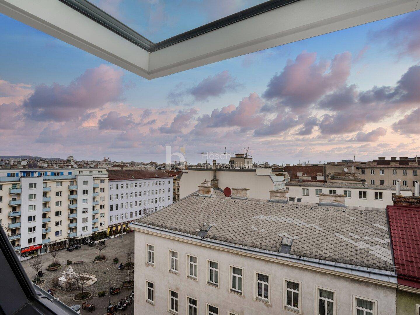 Panoramablick über die Dächer der Stadt bei Sonnenuntergang, gesehen durch ein Dachfenster.