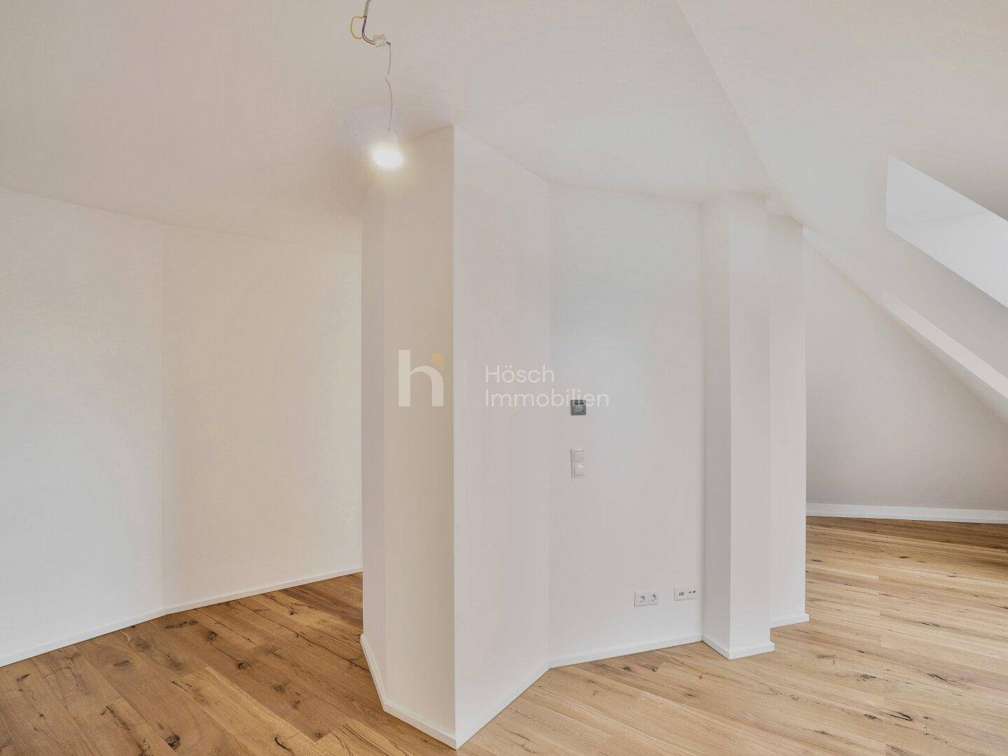 Leerer Raum mit Holzboden, zentralem Pfeiler und Dachschrägen, bereit zur Gestaltung.