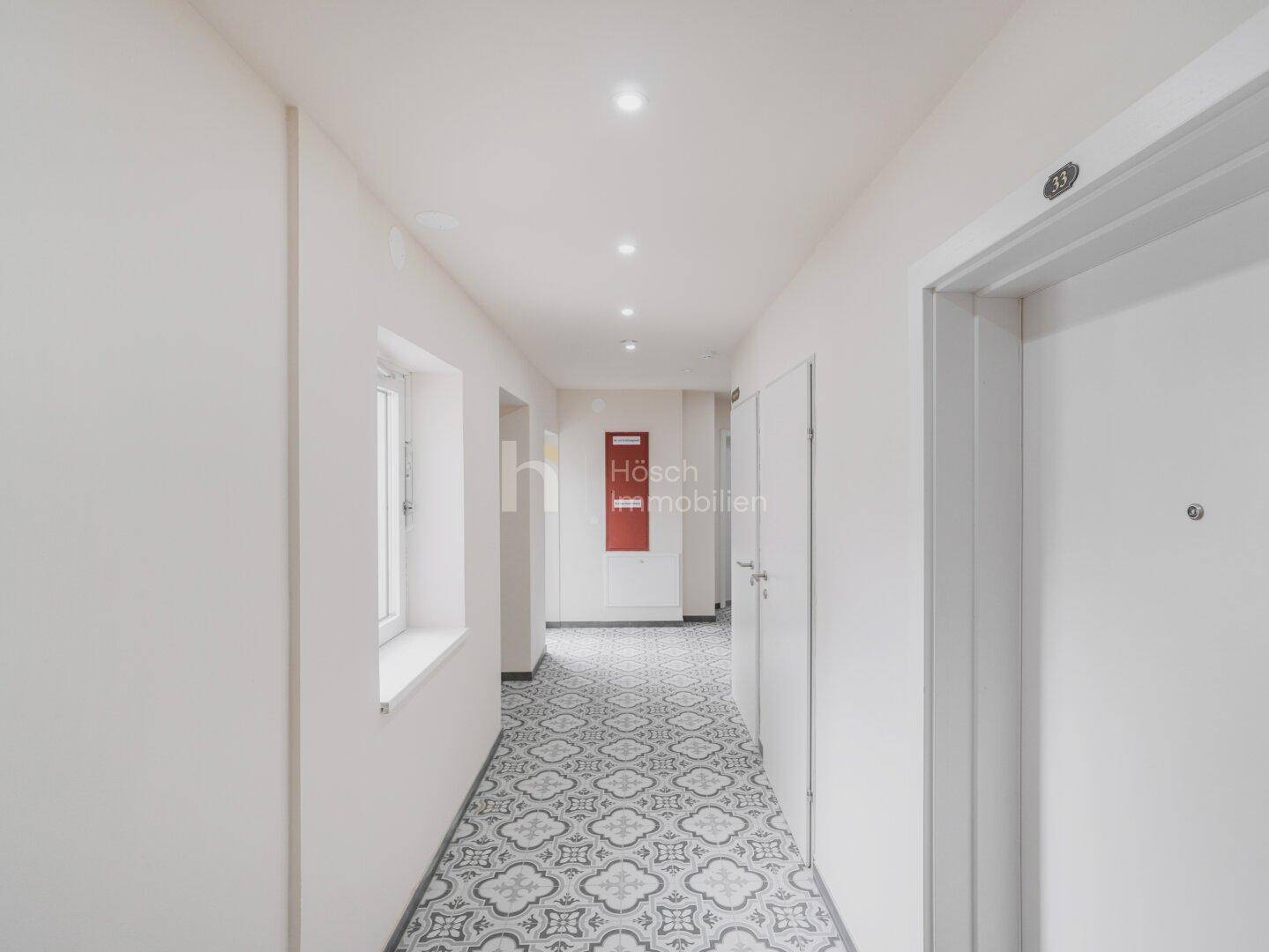 Heller Flur mit gemusterten Fliesen und weißen Wänden, führt zu verschiedenen Räumen der Wohnung.