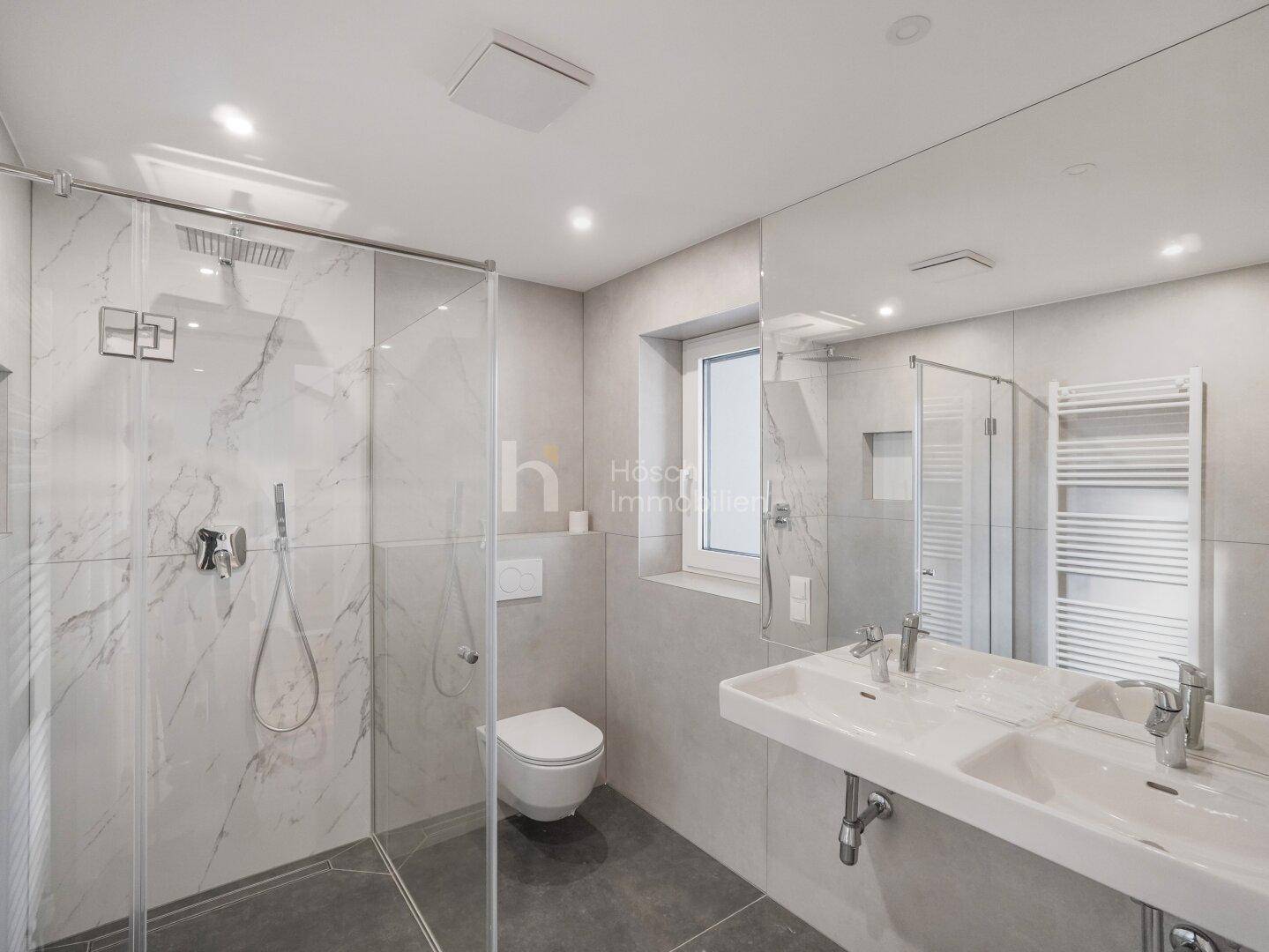 Modernes Badezimmer mit Doppelwaschbecken, großer begehbarer Dusche und Fenster für Tageslicht.