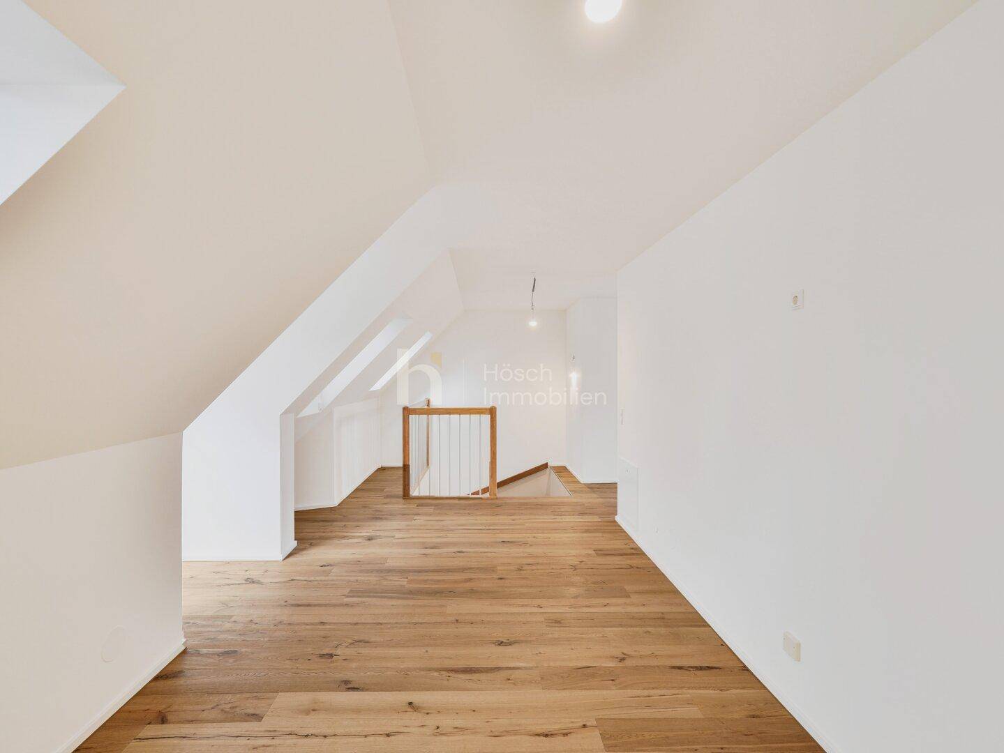 Langer, heller Dachgeschossraum mit Holzboden und schrägen Wänden, bietet vielseitige Nutzungsmöglichkeiten.