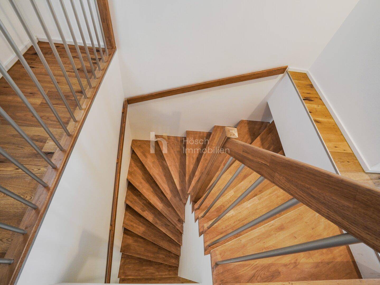 Wendeltreppe aus Holz mit modernen Geländerstäben, verbindet die verschiedenen Ebenen der Wohnung.
