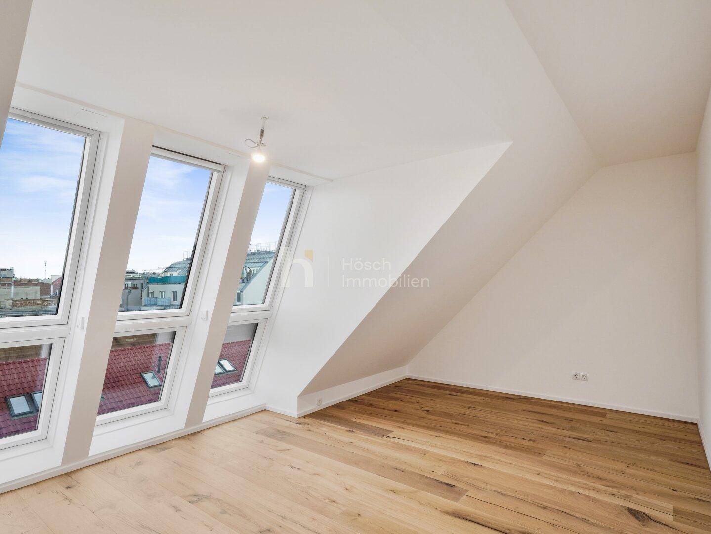 Geräumiger, heller Raum im Dachgeschoss mit Holzboden und breiten Fenstern, ideal für individuelle Gestaltung.