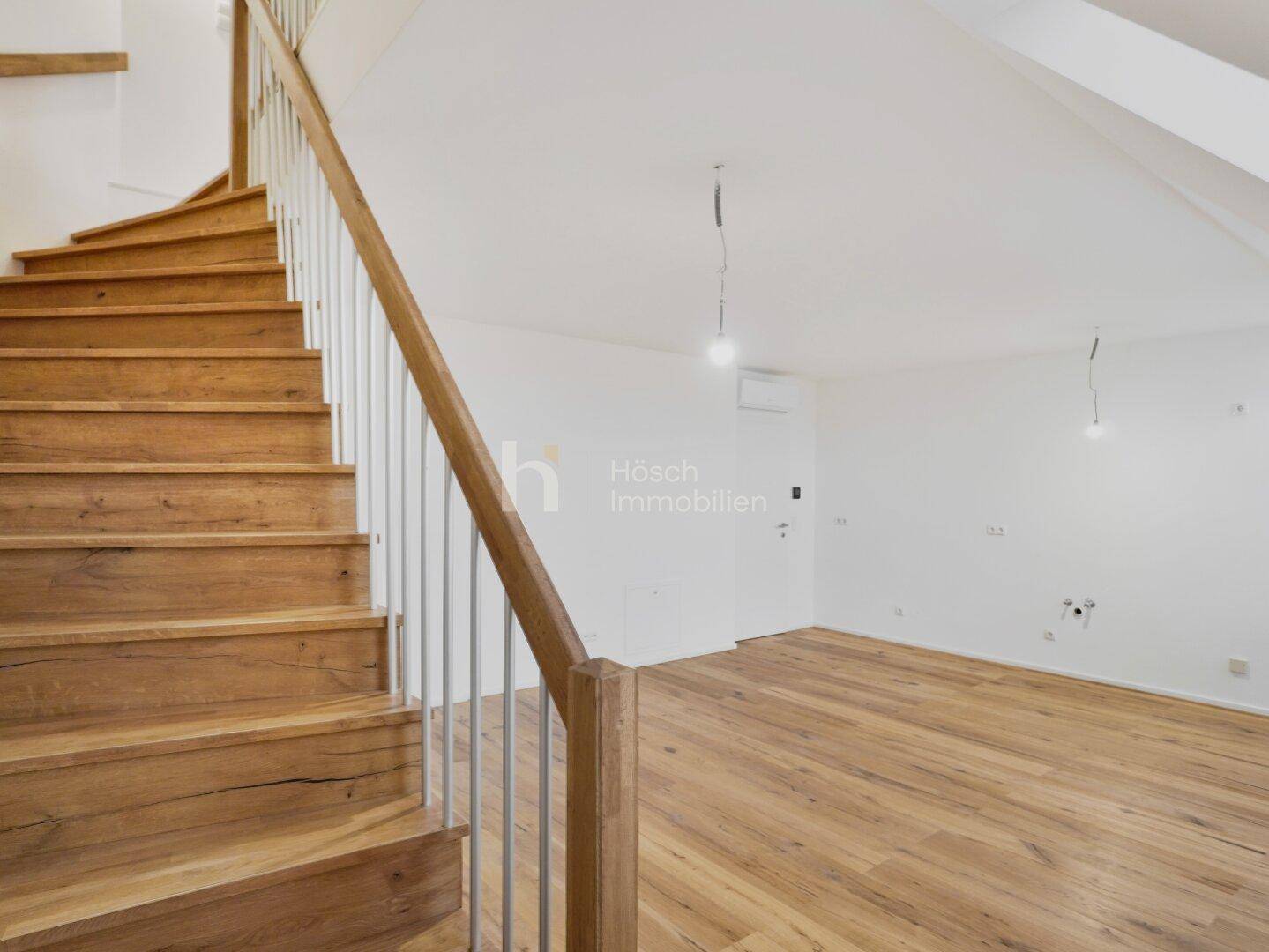 Elegante Holztreppe führt in einen hellen Raum im Dachgeschoss mit Holzboden und schrägen Wänden.