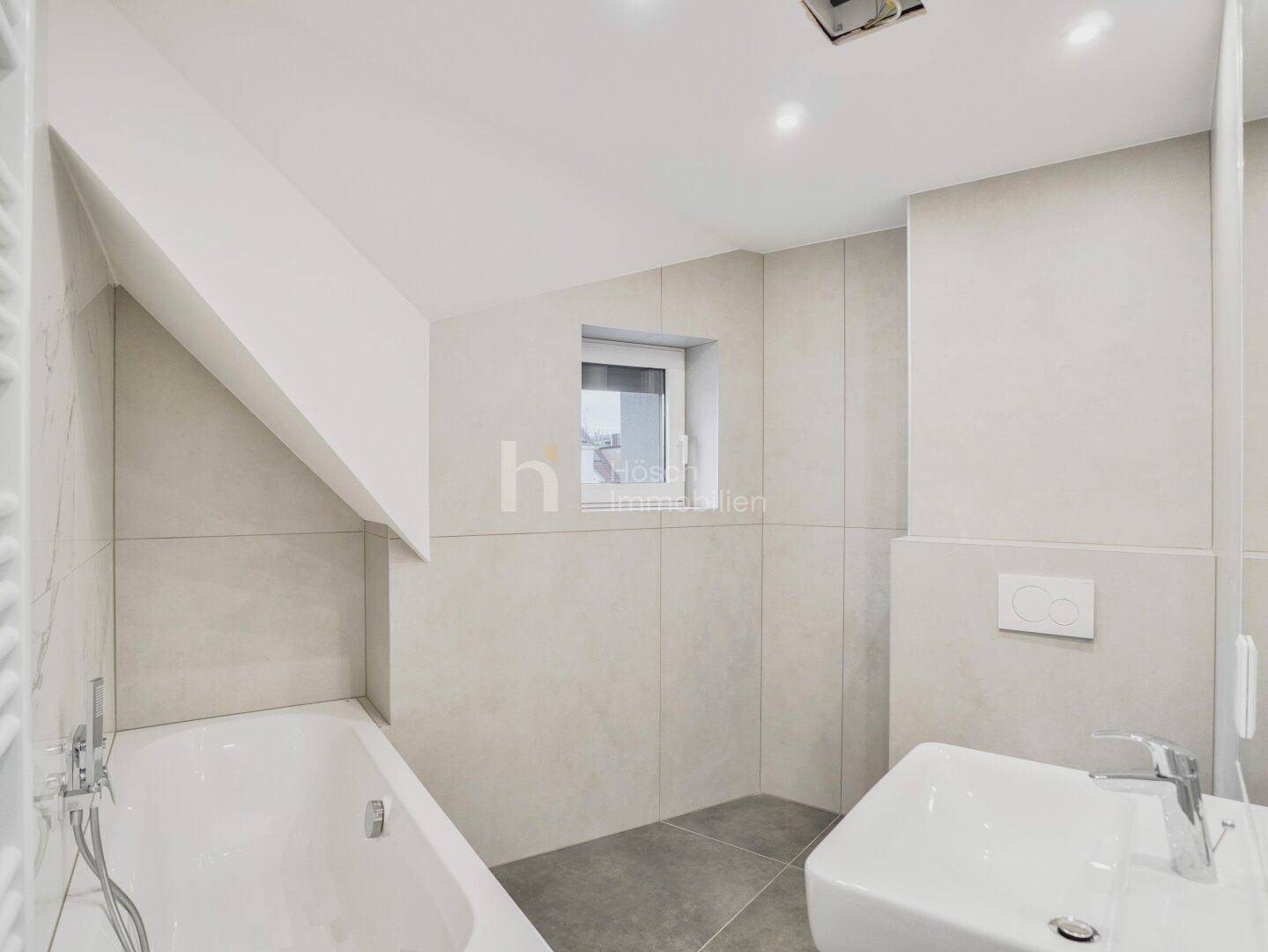 Helles Badezimmer im Dachgeschoss mit Badewanne, Einzelwaschbecken und Fenster für natürliche Belüftung.