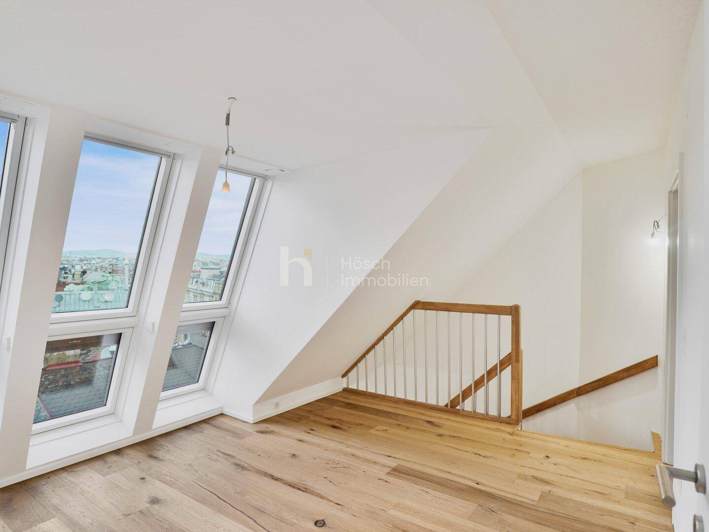 Heller Raum im Dachgeschoss mit Holzboden, großen Dachfenstern und Treppenzugang zu weiteren Ebenen.