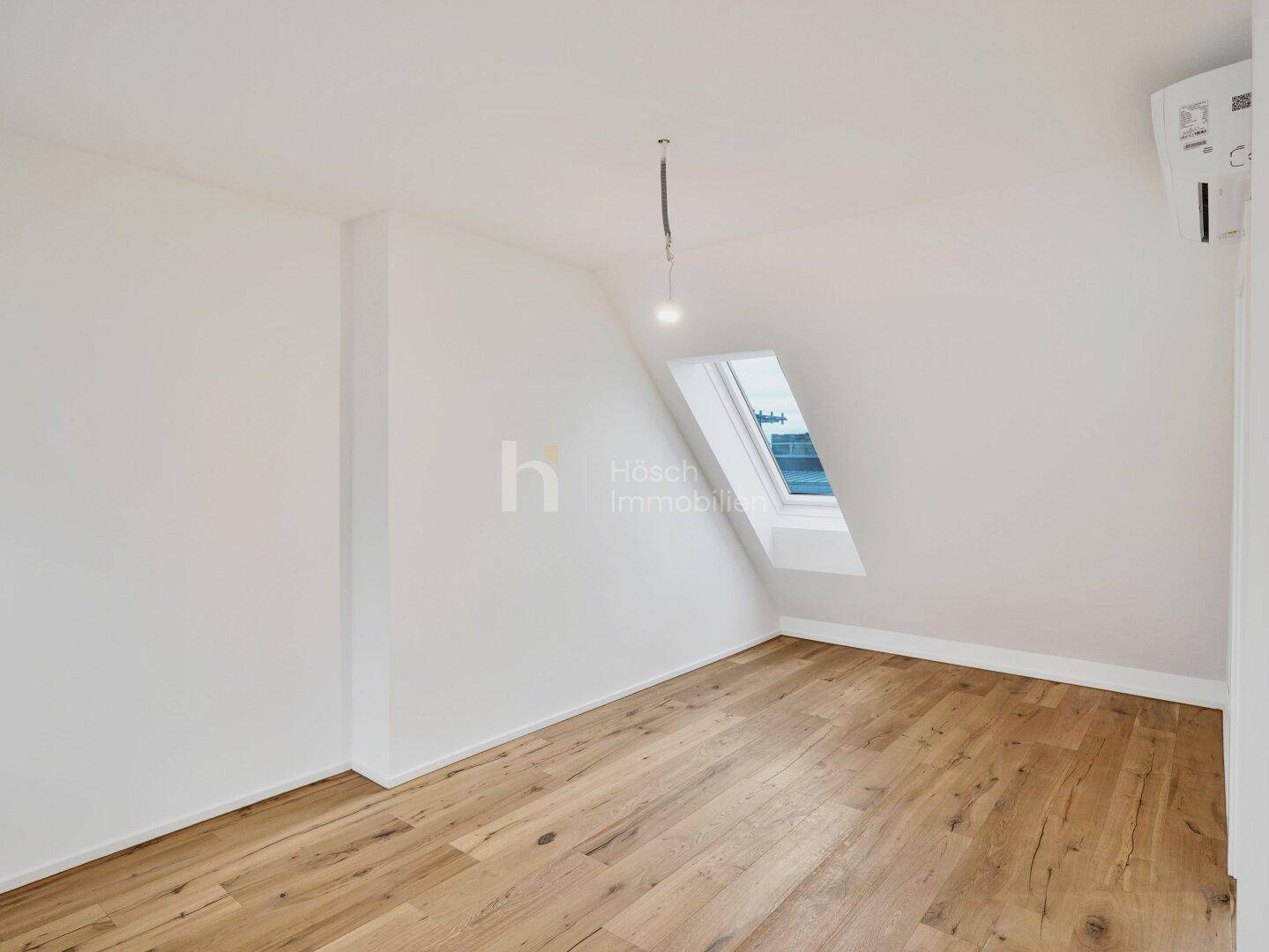 Leerer Raum im Dachgeschoss mit Holzboden, einem Dachfenster und installierter Klimaanlage für Komfort.