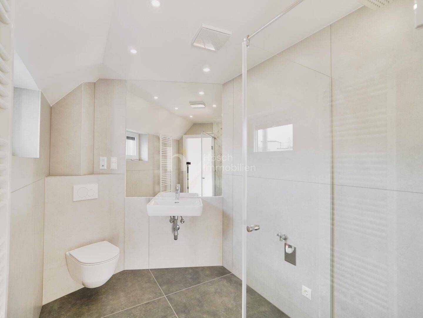 Modernes Badezimmer mit Duschkabine, Wand-WC, Einzelwaschbecken und hellen, großformatigen Fliesen.