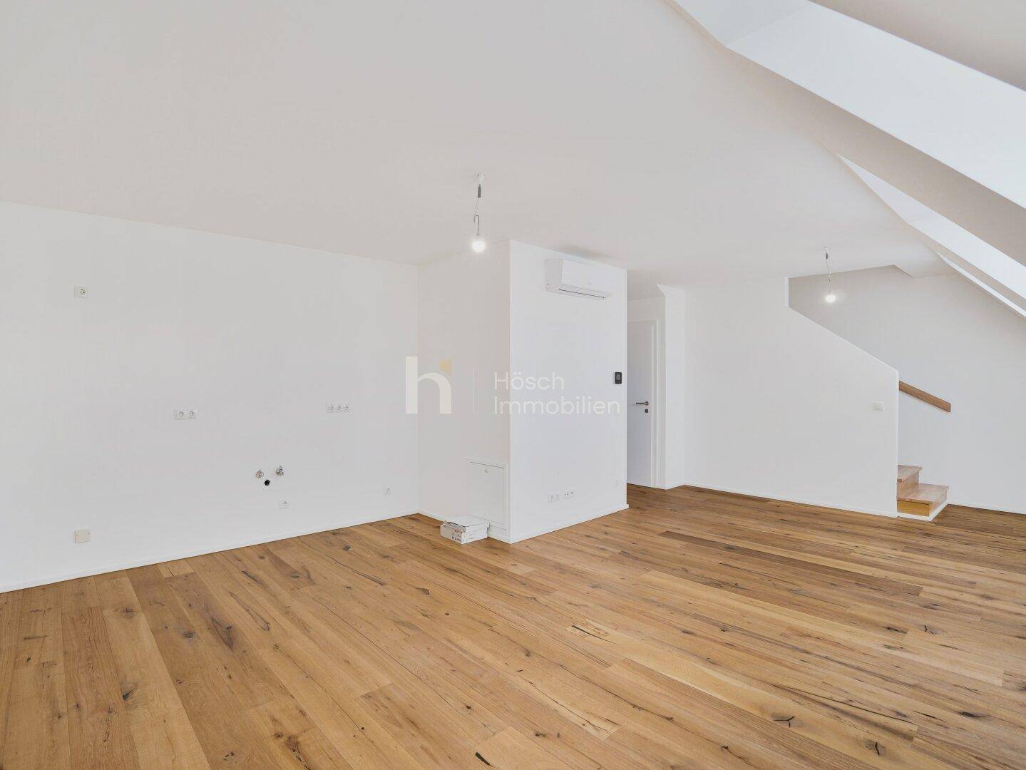 Heller Raum mit Holzboden, Klimaanlage und Zugang zu einer Treppe, die in weitere Bereiche führt.