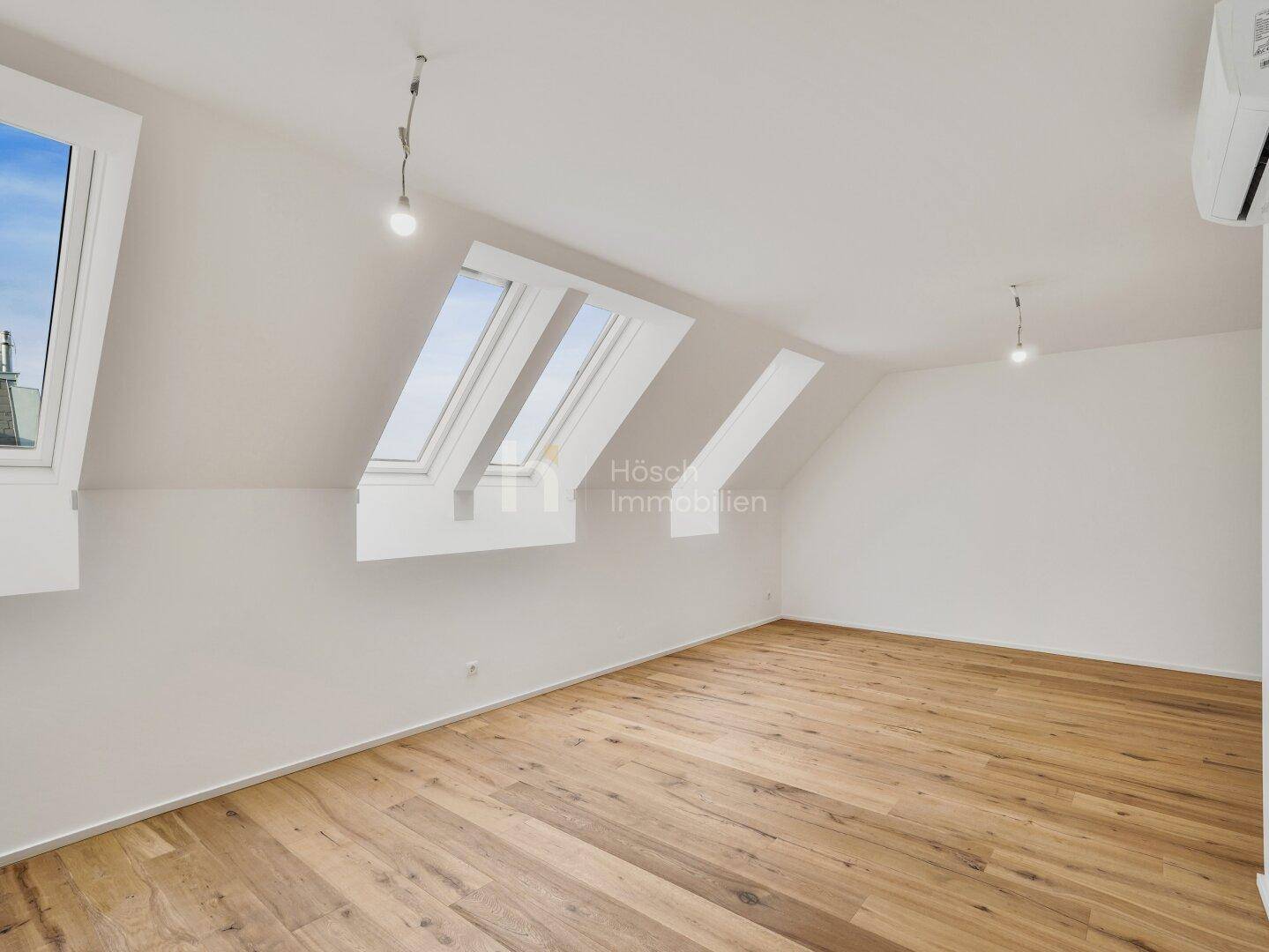 Helles Zimmer im Dachgeschoss mit Holzboden und zwei Dachfenstern, bietet viel natürliches Licht.