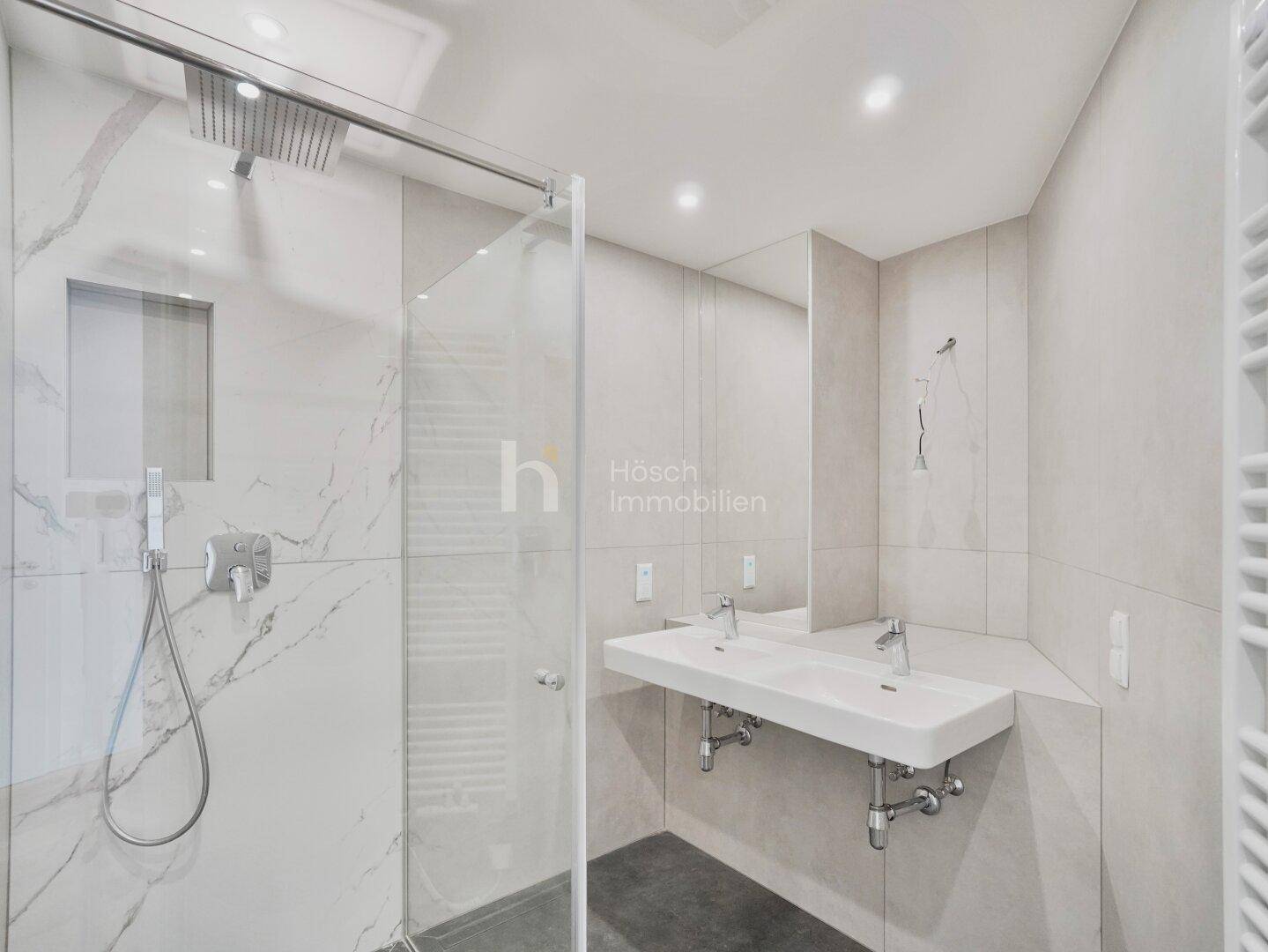 Elegantes Badezimmer mit Doppelwaschbecken, großer Regendusche und hochwertigen Fliesen in Marmoroptik.