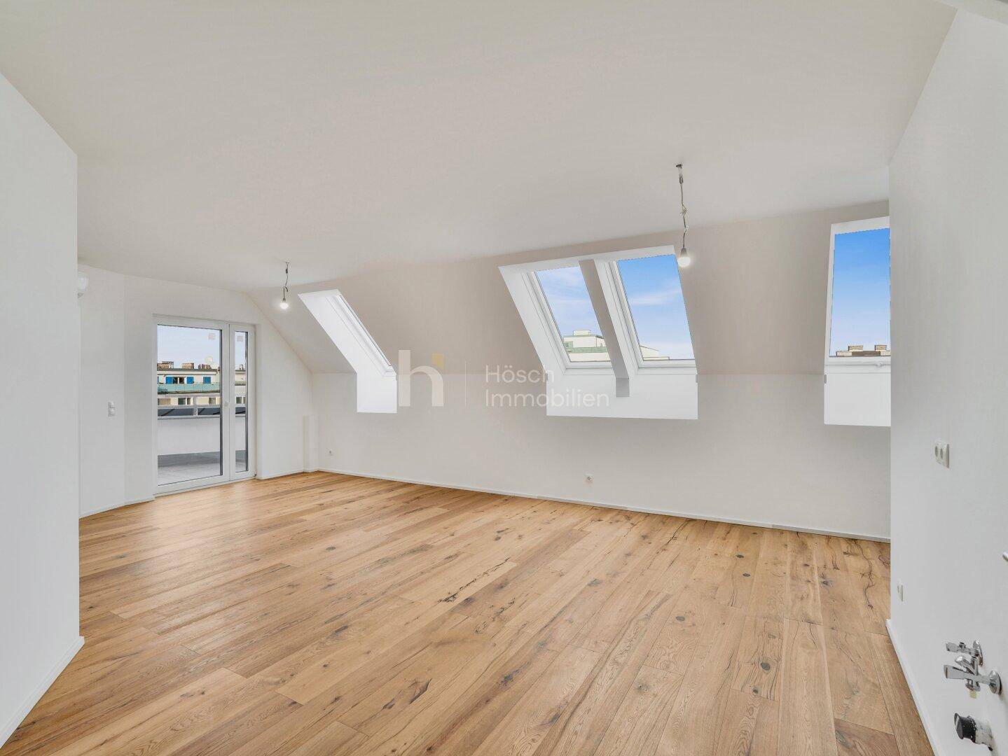 Großzügiger Dachgeschossraum mit Holzboden, Dachfenstern und direktem Zugang zu einem Balkon.