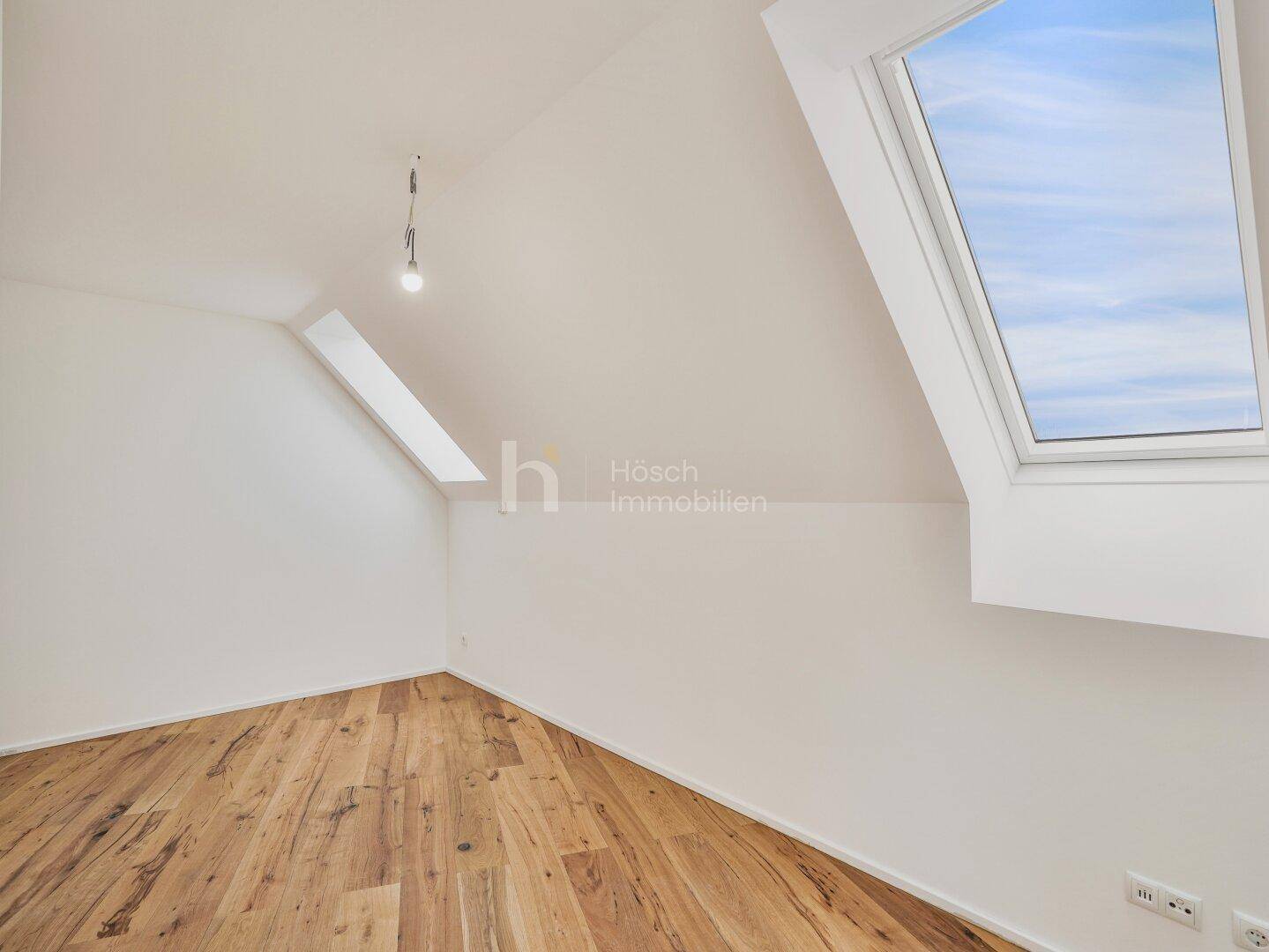 Ruhiger Dachgeschossraum mit Holzboden und einem großen Dachfenster, das viel Tageslicht hereinlässt.