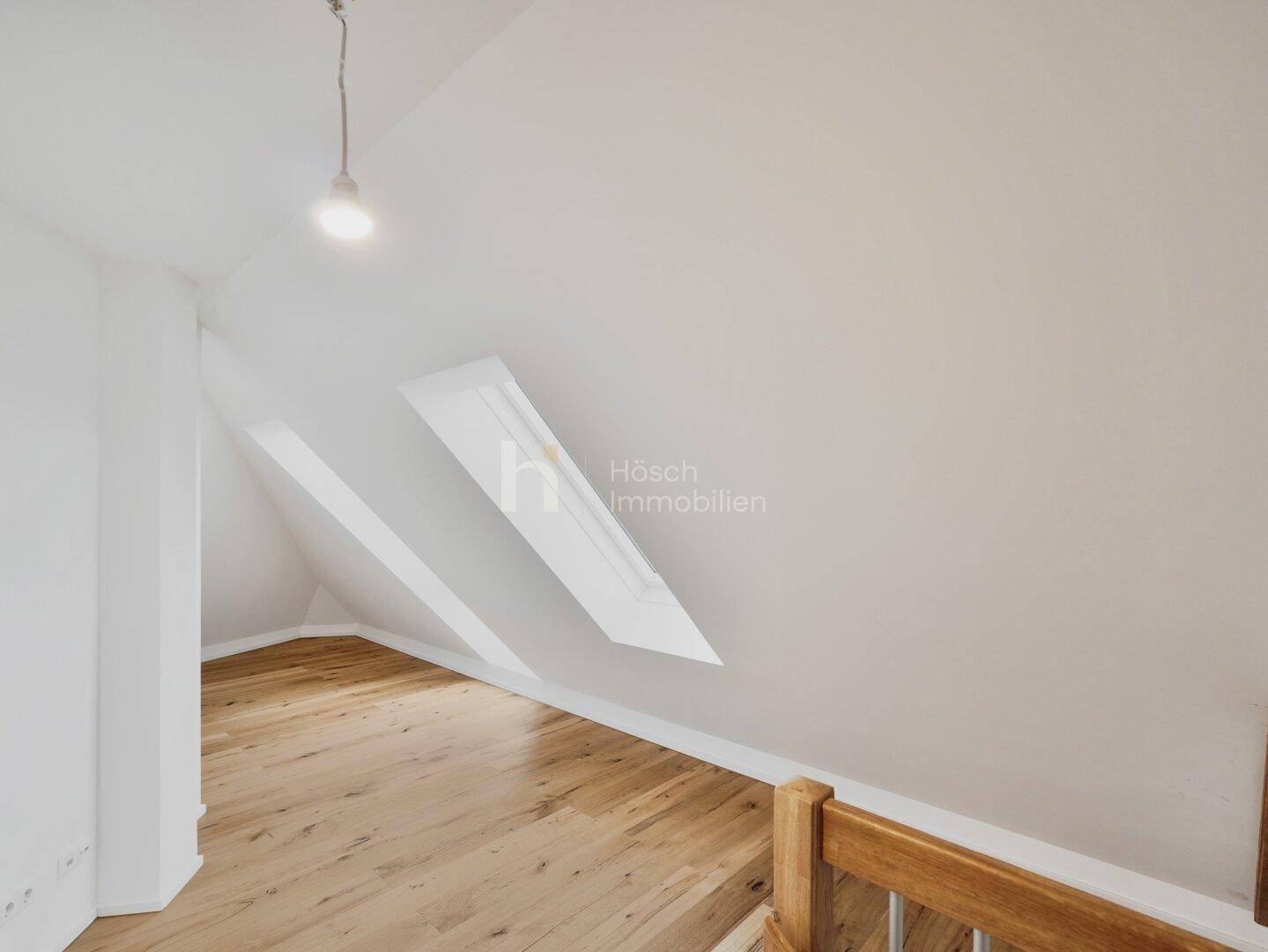 Heller Dachgeschossraum mit Holzboden, mehreren Dachfenstern und einem Treppenzugang zu weiteren Ebenen.