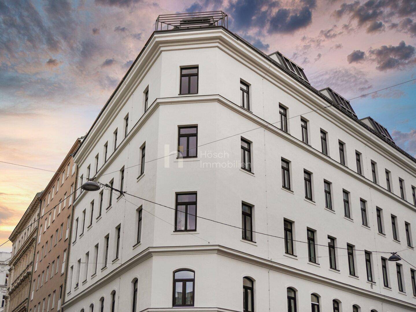 Elegante weiße Fassade eines modernen Gebäudes mit vielen Fenstern unter einem dramatischen Himmel.