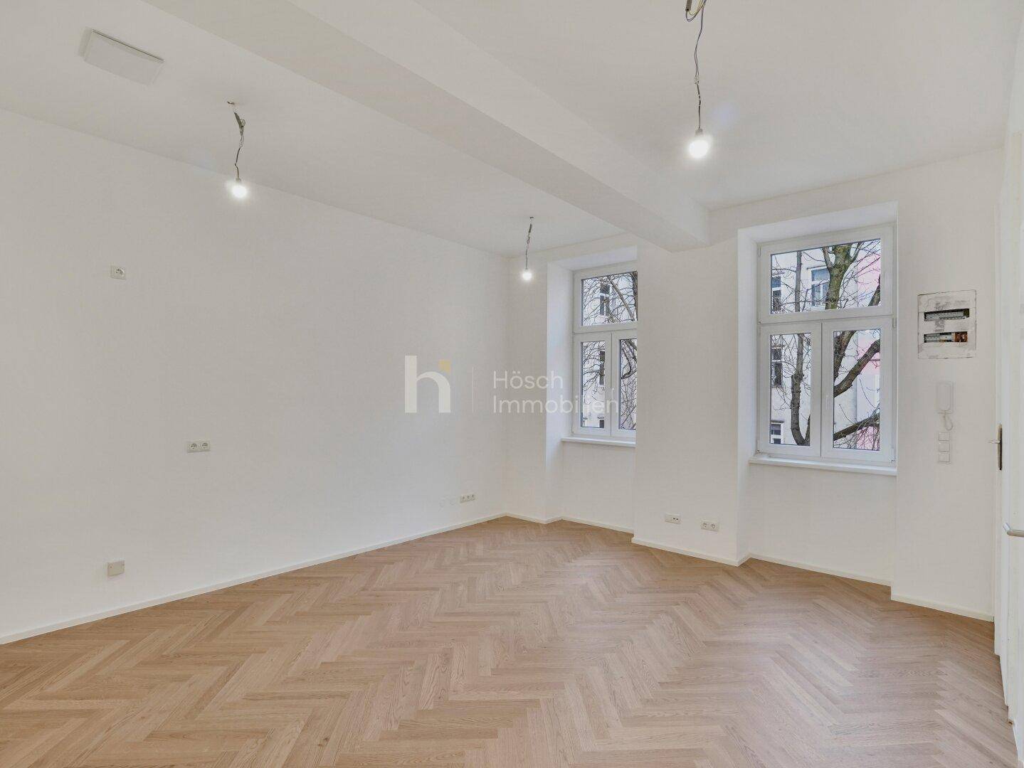Geräumiges Zimmer mit Fischgrätparkett und hohen Decken, ideal für Wohn- oder Schlafbereich.