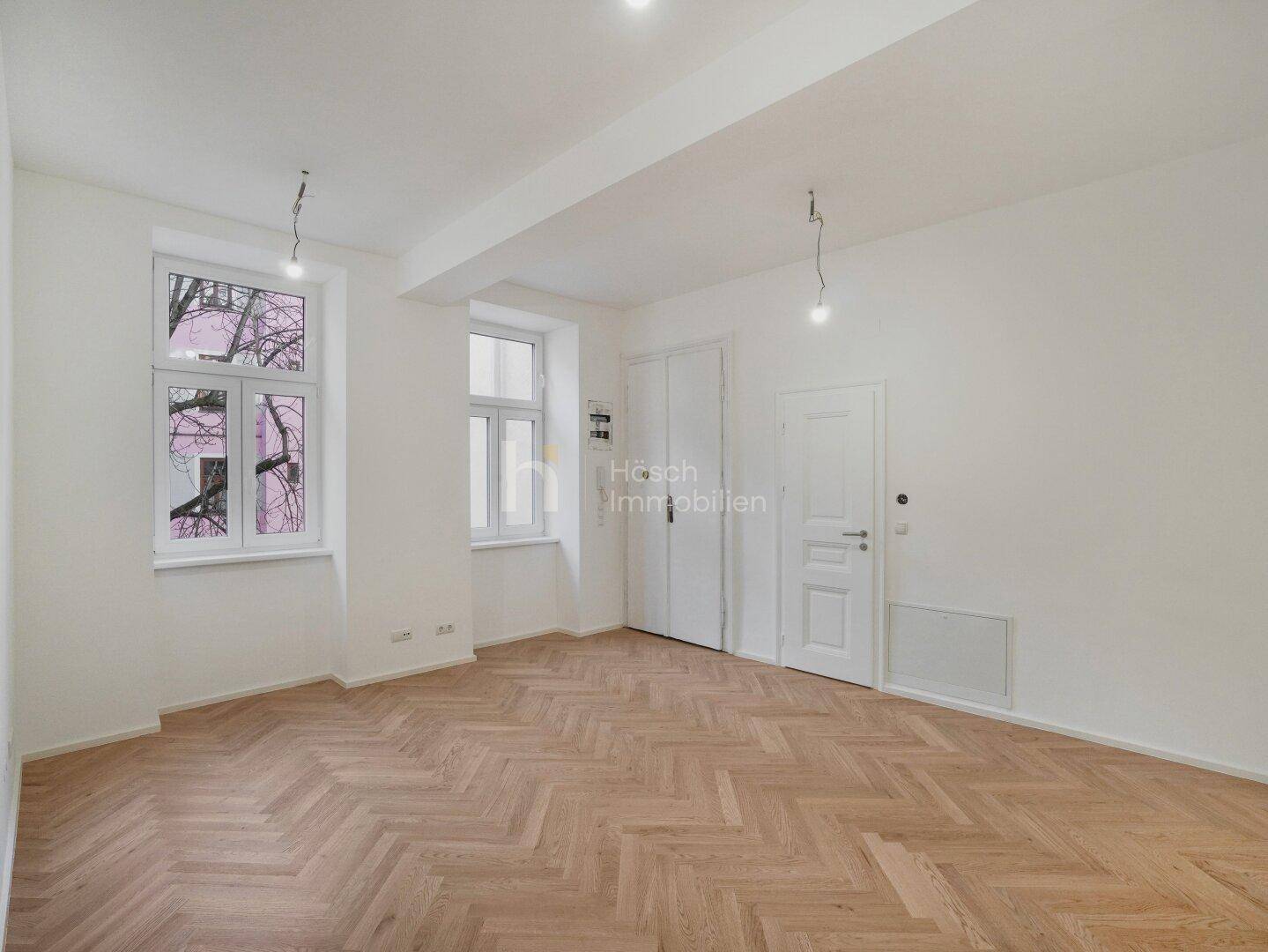 Lichtdurchflutetes Zimmer mit klassischem Fischgrätparkett und weiß gestrichenen Wänden.