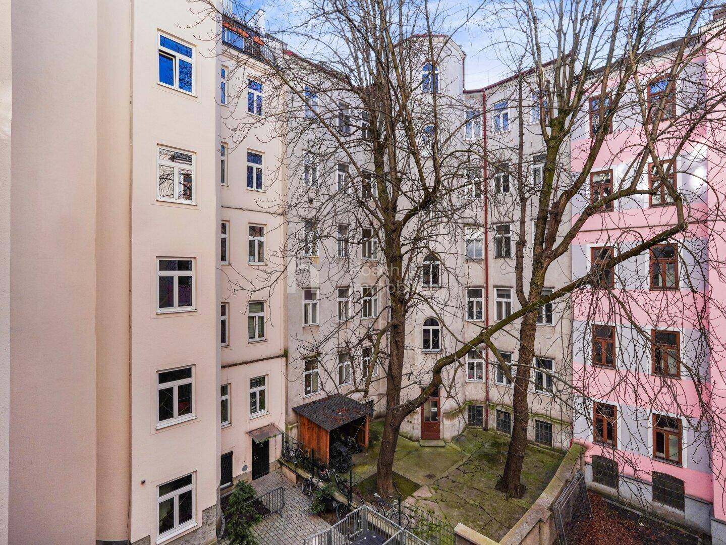Ruhiger Innenhof mit Bäumen und gepflastertem Bereich, umgeben von Wohngebäuden.