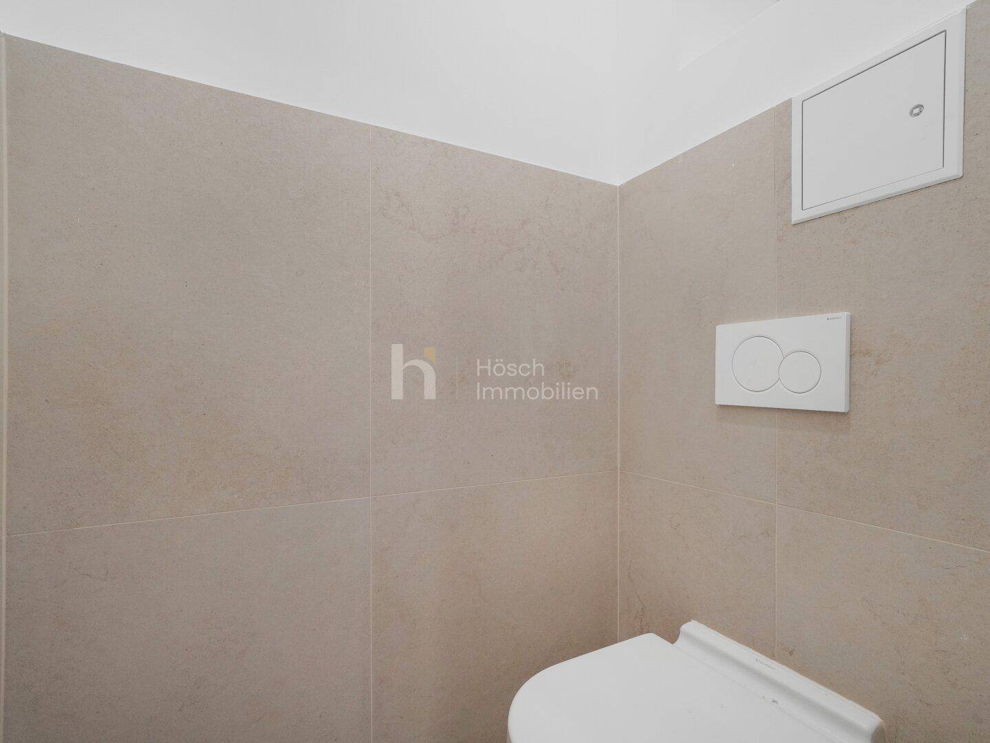 Separates WC mit hellen Fliesen und wandmontierter Spülung, sauber und funktional.